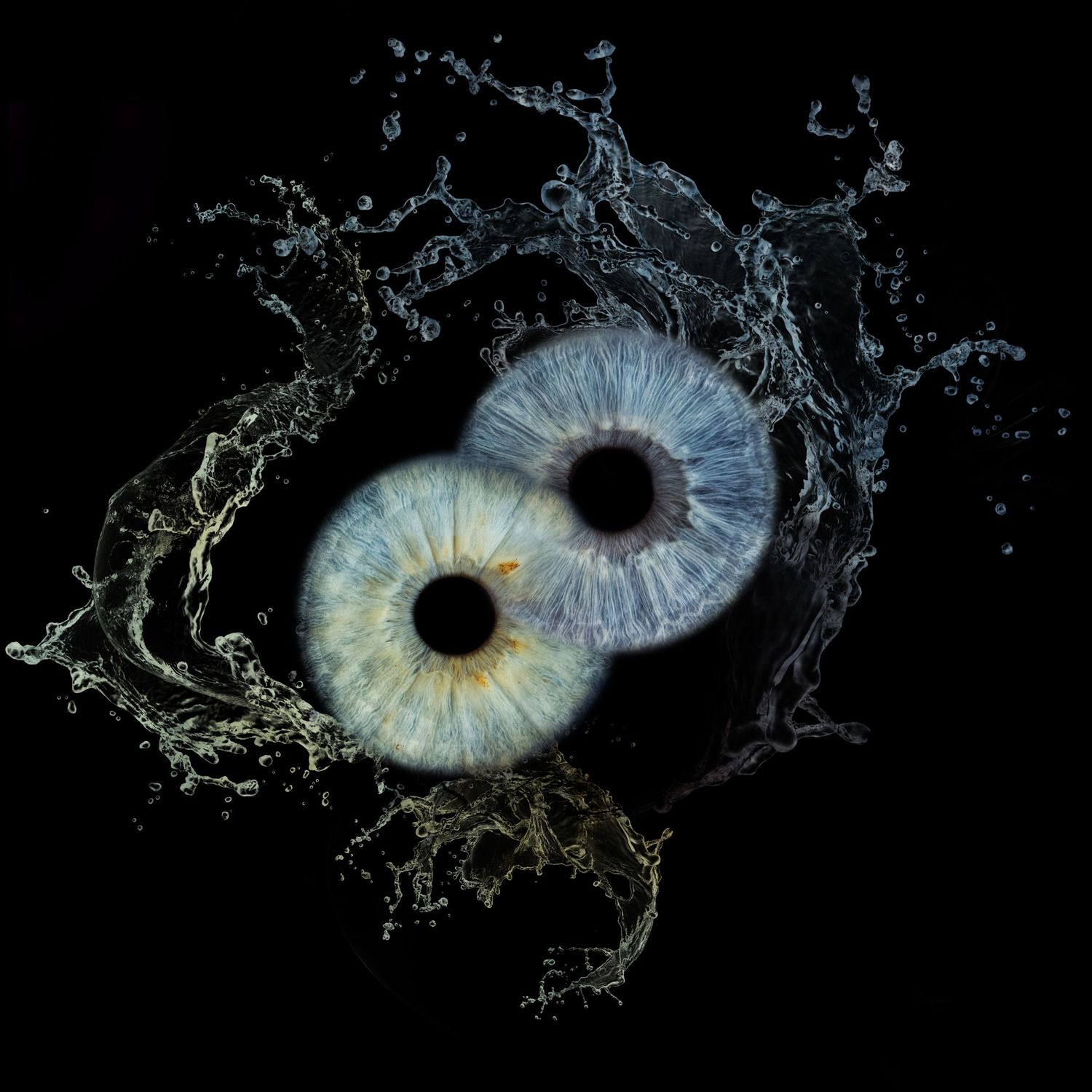 Two human irises with blue and hazel tones surrounded by dramatic water splashes on a dark background.