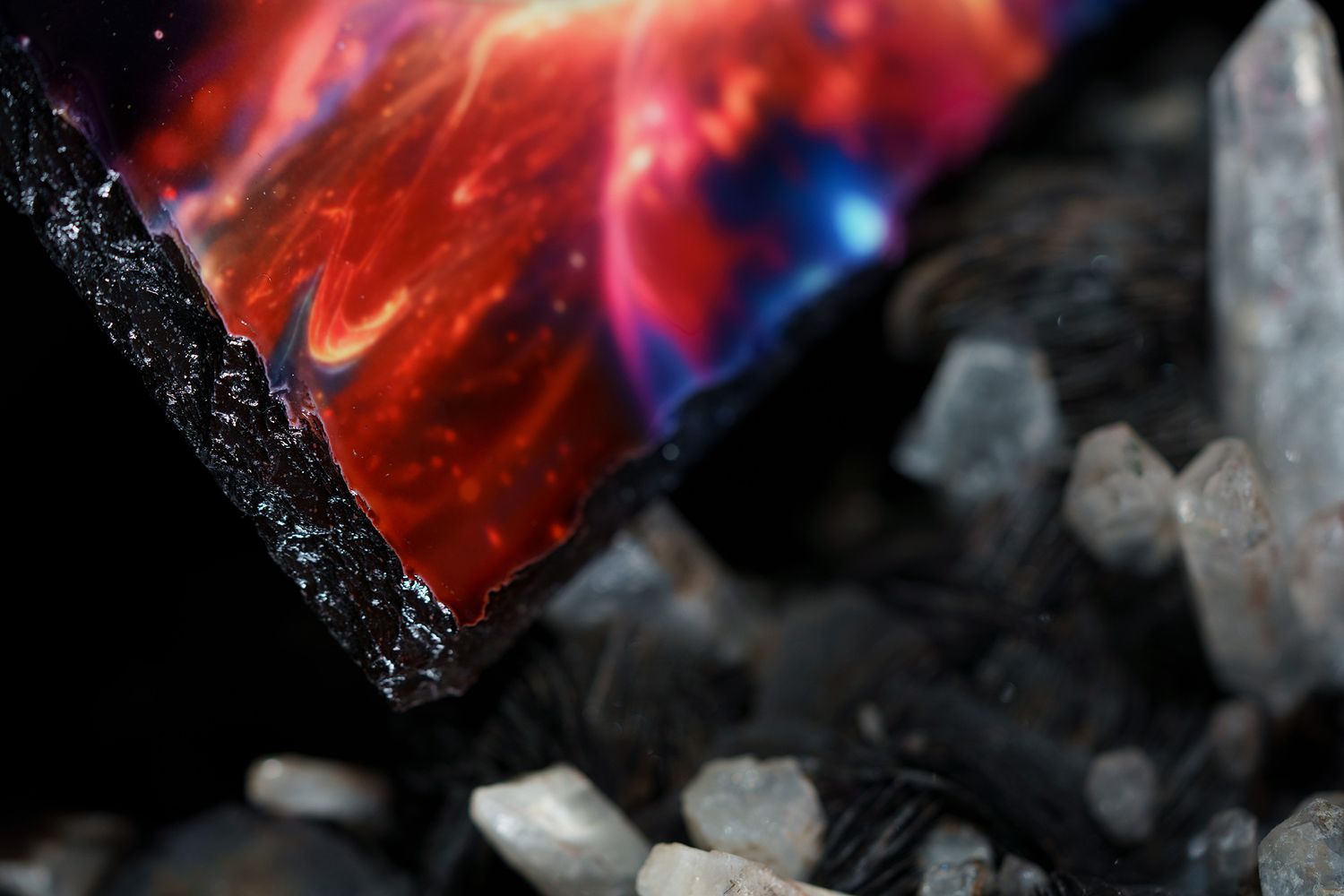 Dark mineral crystals contrast against a vibrant red and blue glowing object in extreme macro photography.
