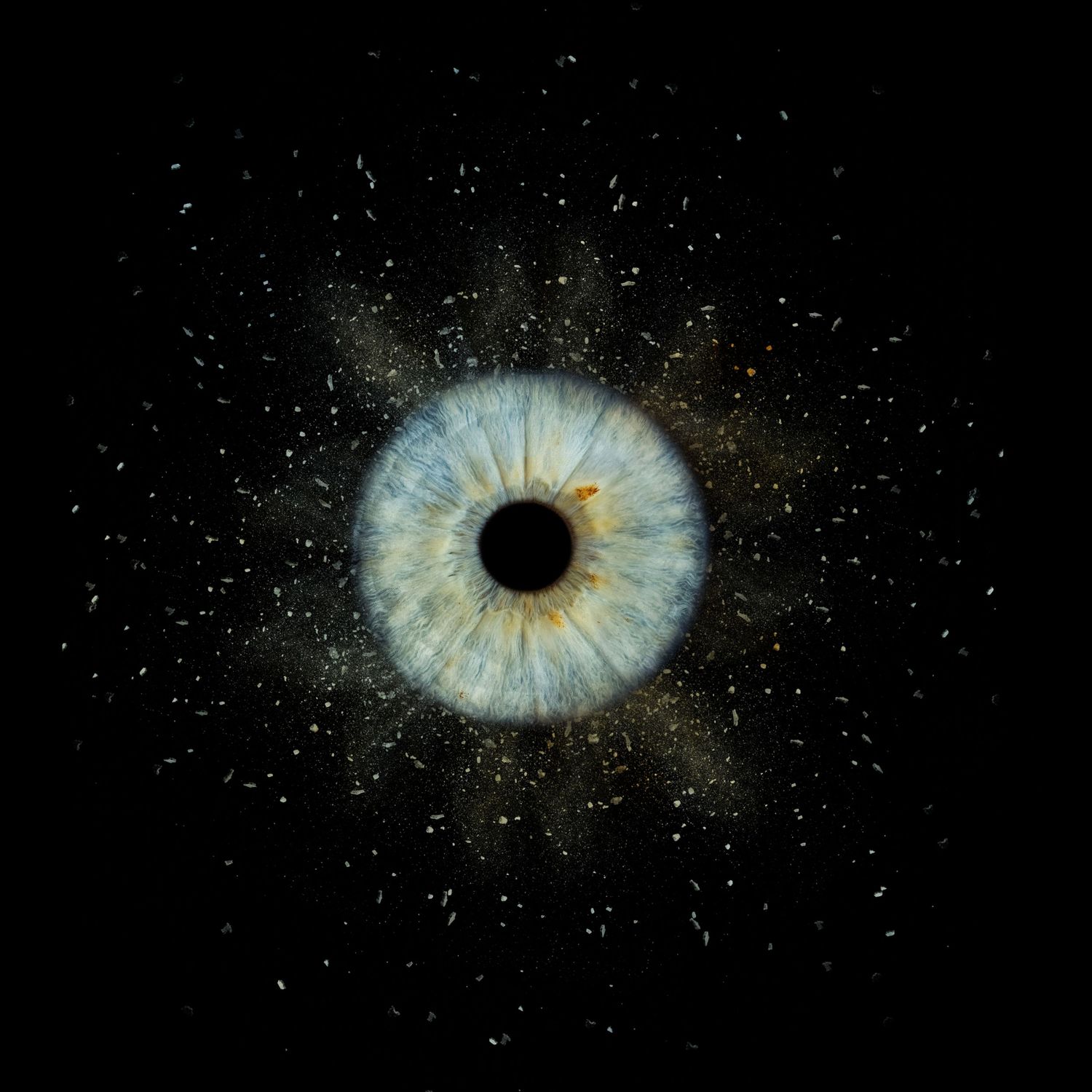 Macro photo of a blue human eye surrounded by scattered particles on a dark background.