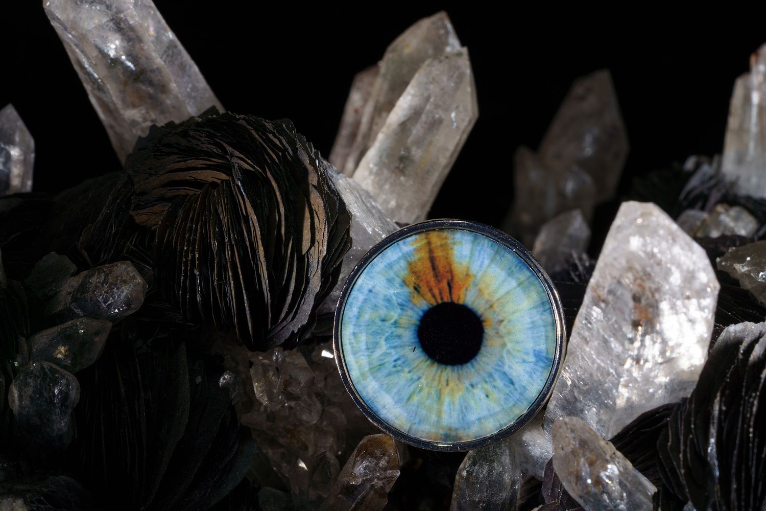 A bright blue glass eye rests among clear quartz crystals and dark shiny spheres.