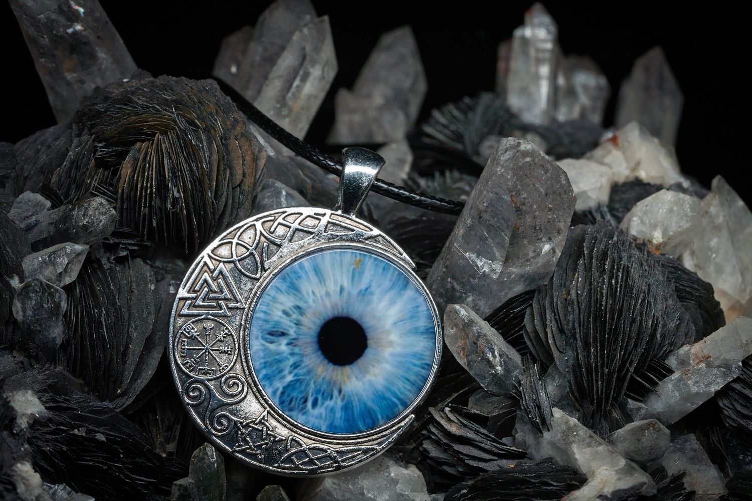 Ornate silver pendant with blue glass eye design rests on dark crystals and black tourmaline stones.