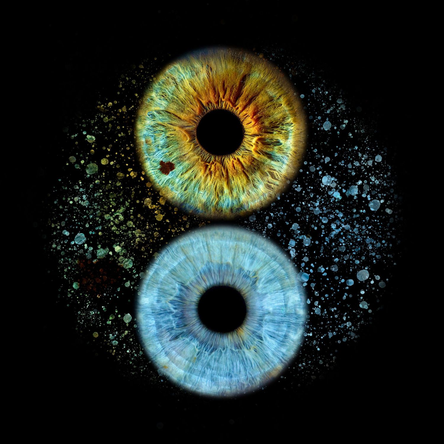 Two iridescent human irises, one amber gold and one ice blue, with sparkling particles against a black background.