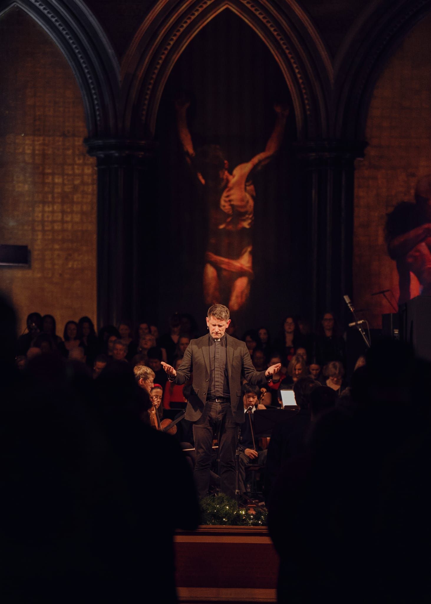 Conductor performing in a grand church with a crucifix and choir in background.