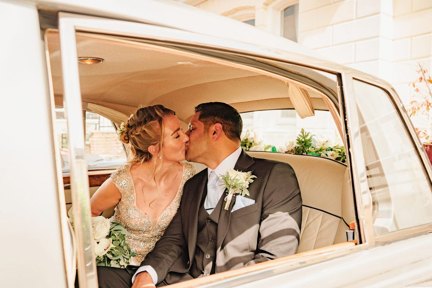 Bride and groom sharing a romantic kiss inside a classic vintage wedding car.