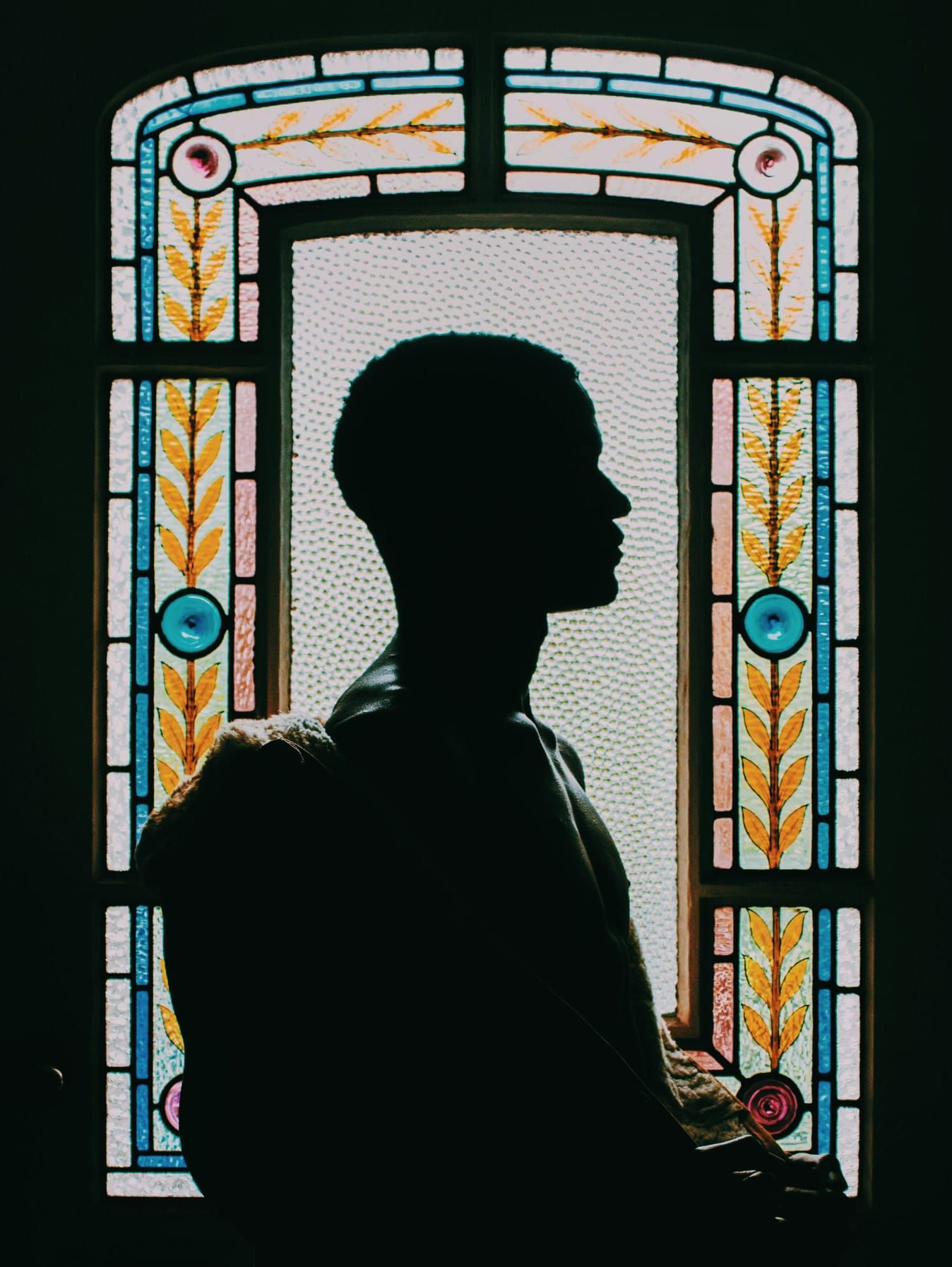 Silhouette of person profile against colorful stained glass window with floral design.