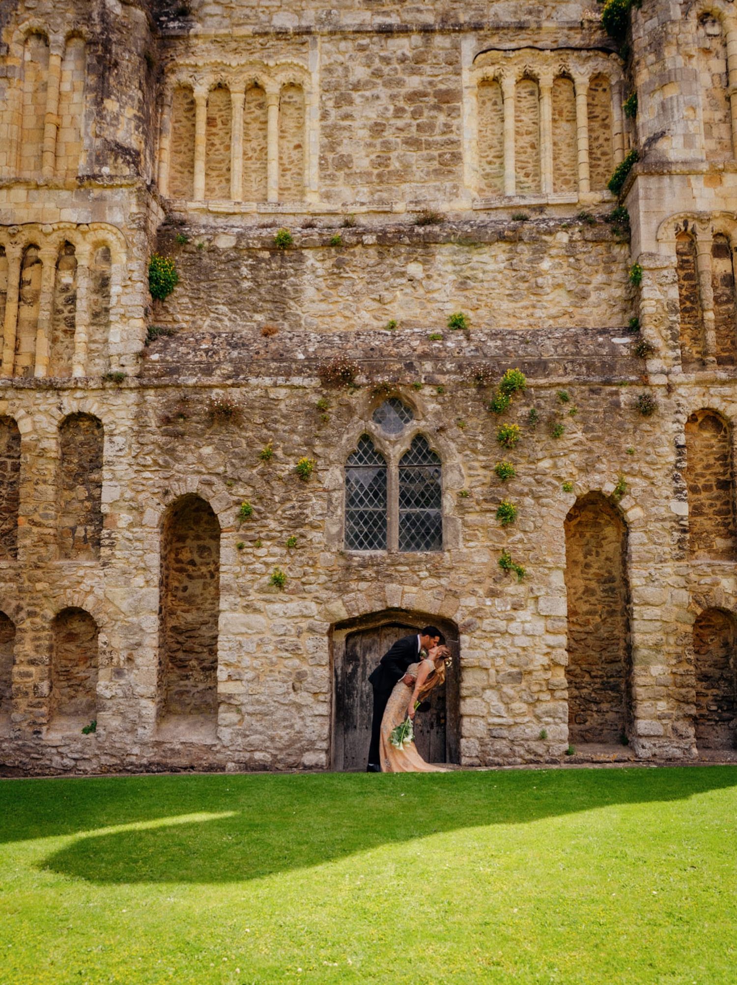 A couple shares a romantic kiss in the arched doorway of an ancient stone castle.