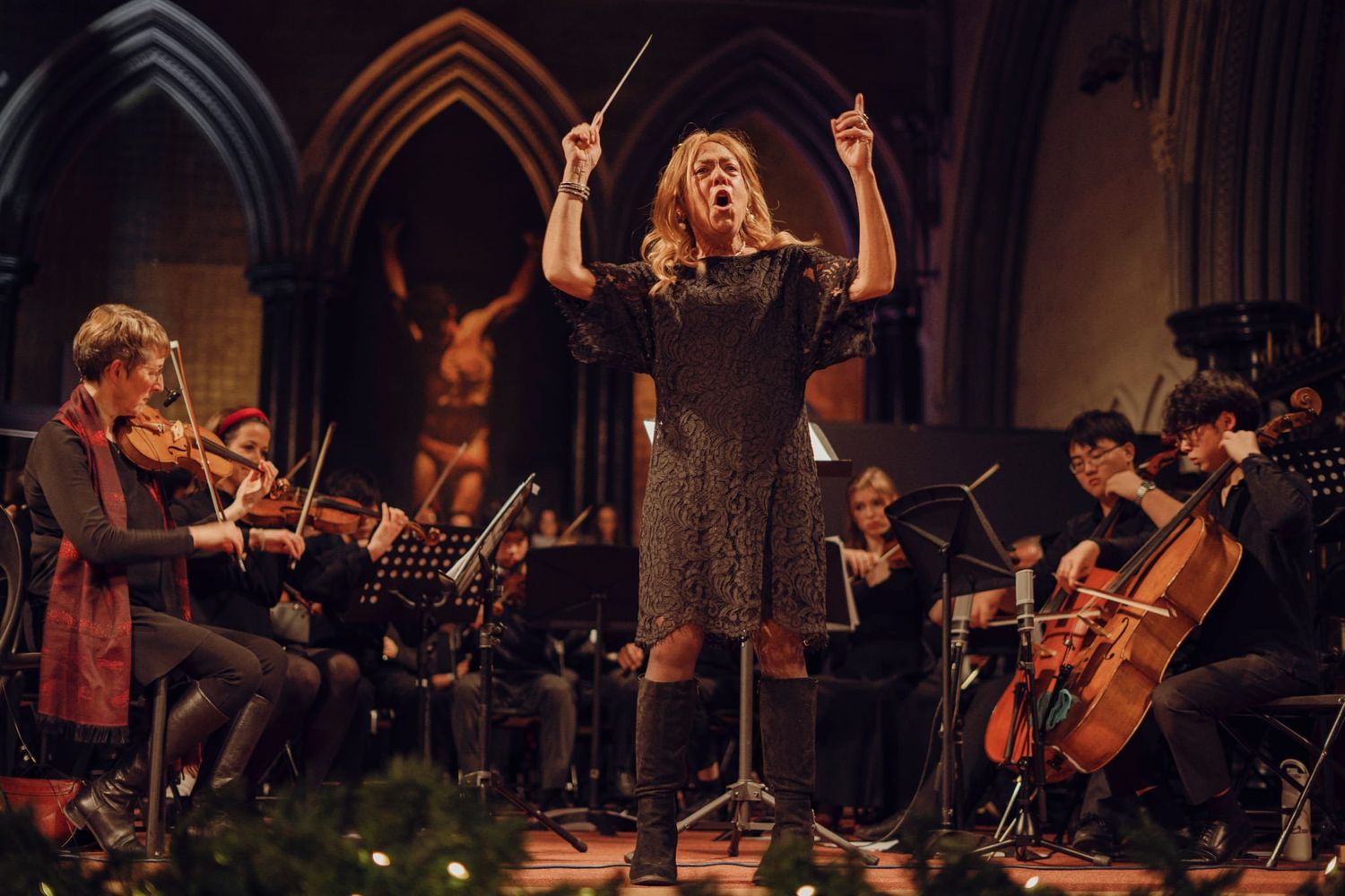 Female conductor leading orchestra in a decorated church Christmas concert.
