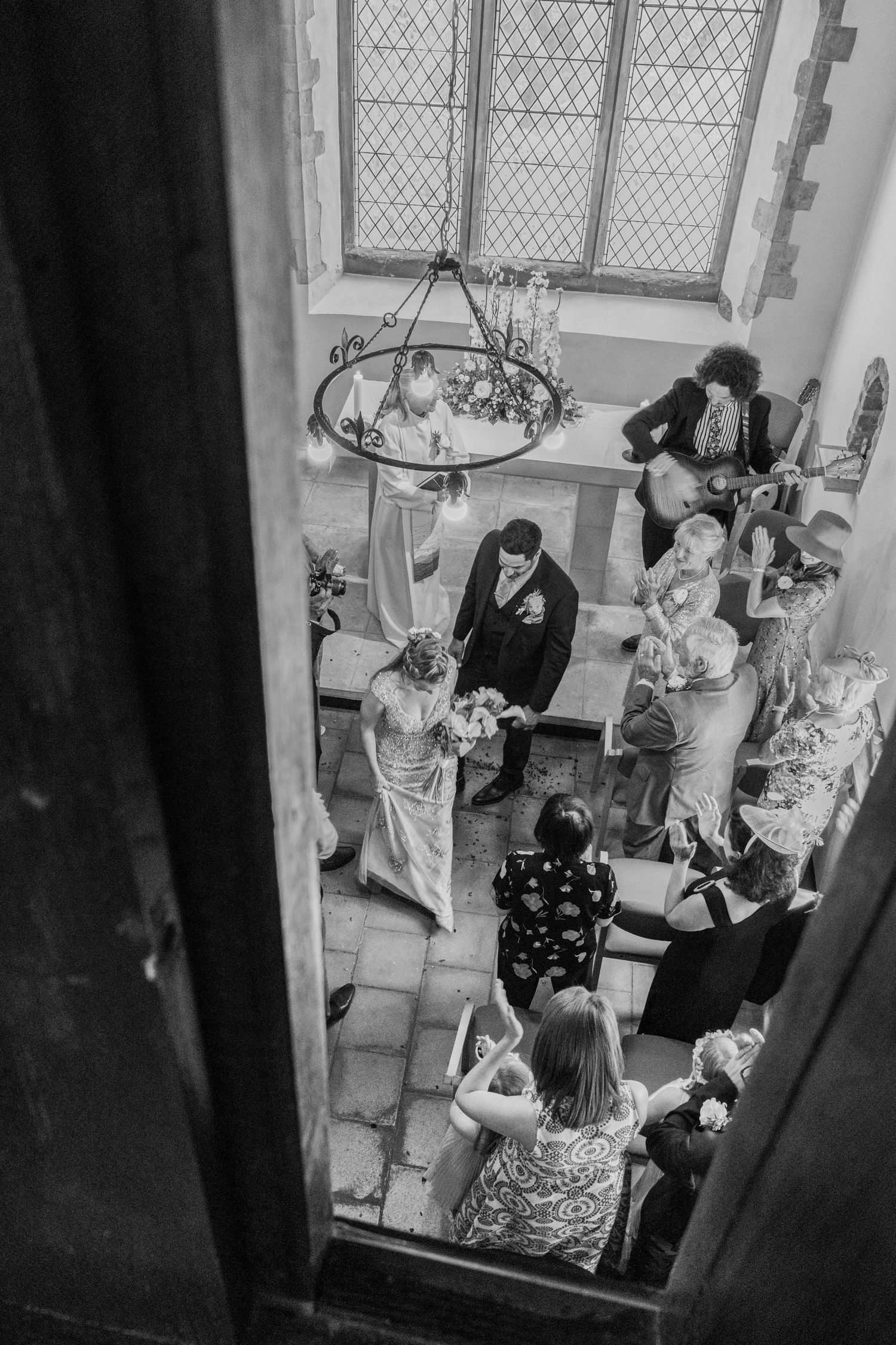 Aerial black and white view of wedding ceremony inside a historic church with guests gathered around couple.
