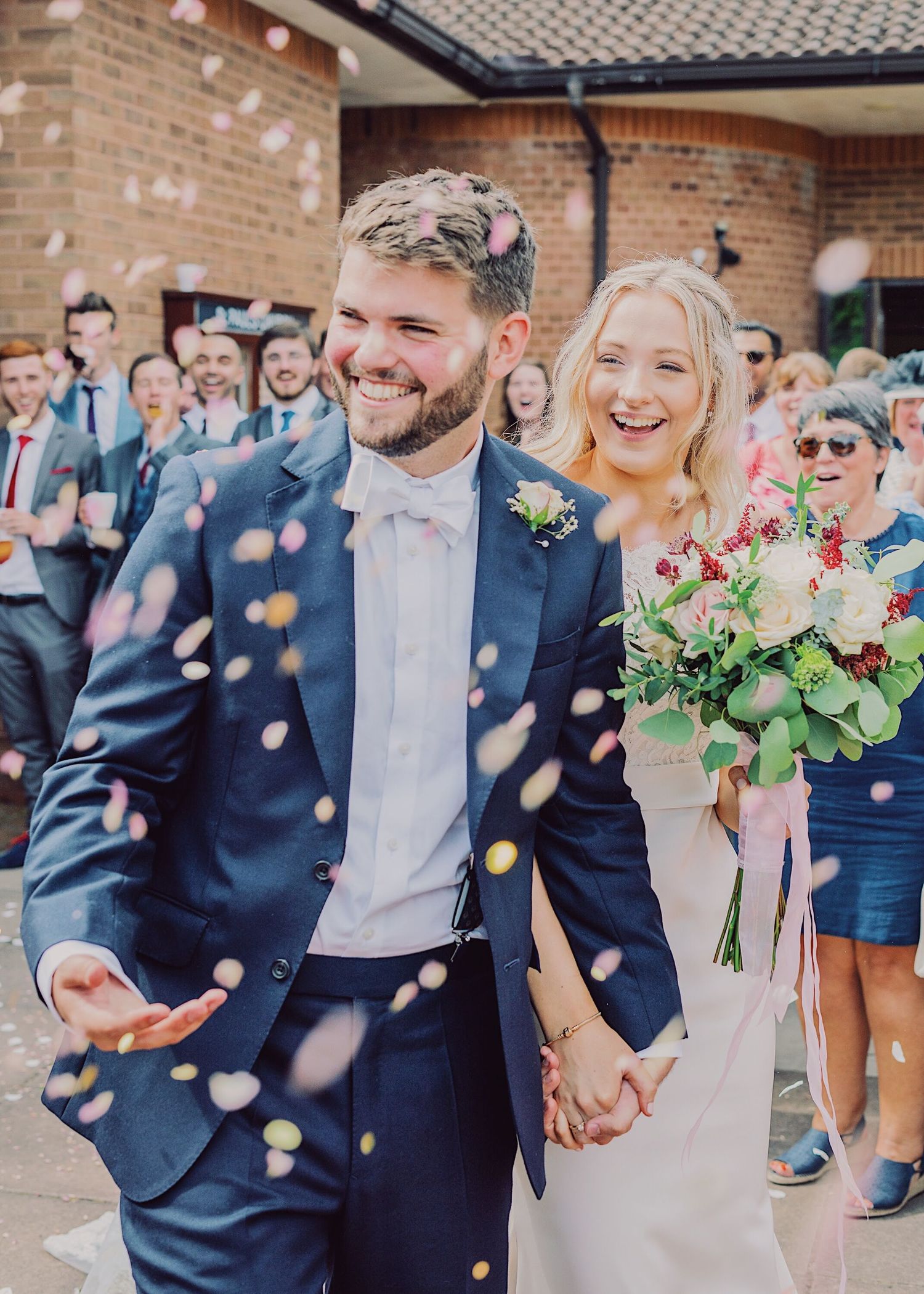 Happy couple laughing as colorful confetti falls during joyful outdoor wedding ceremony exit.
