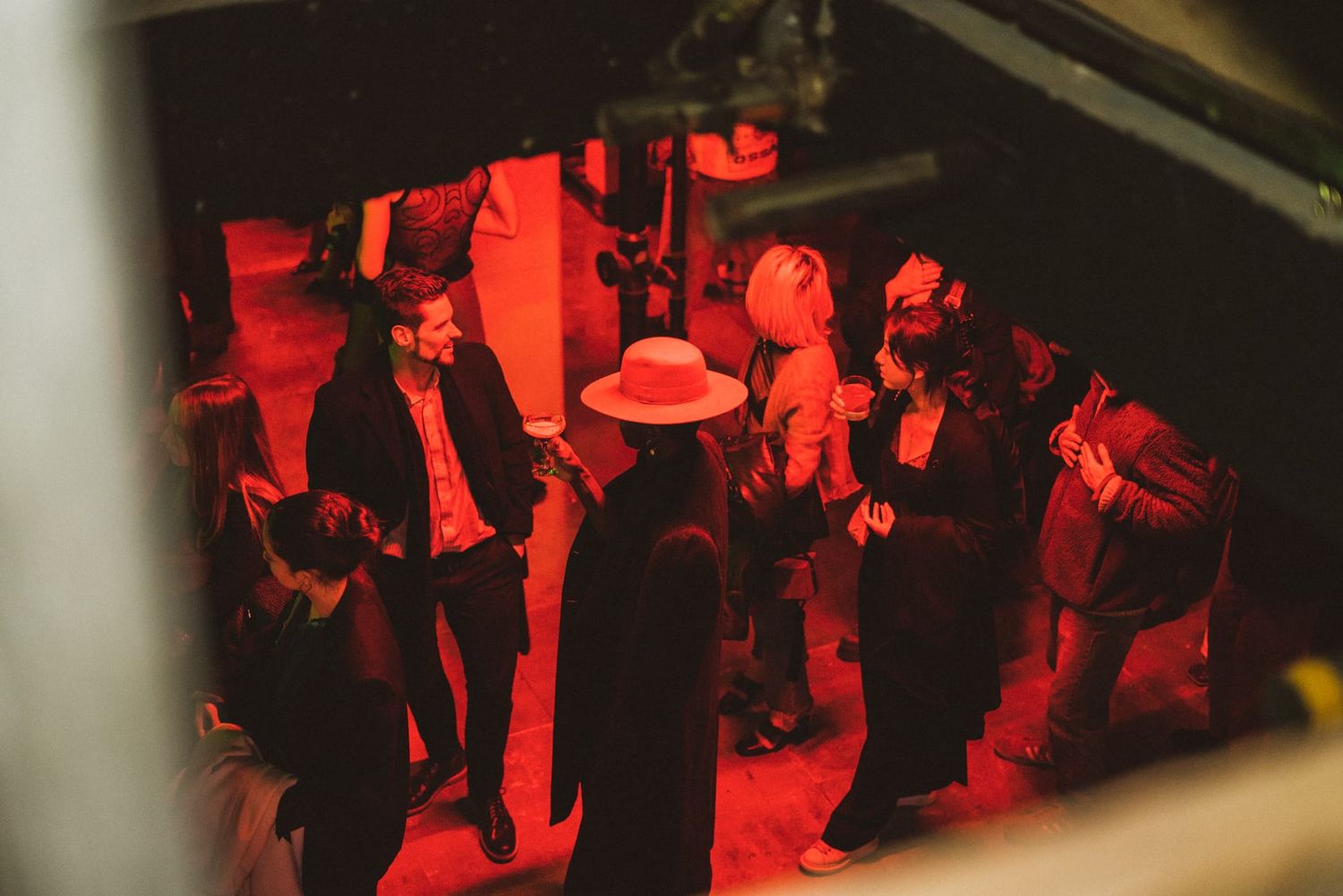 Overhead view of guests socializing under red lighting at an indoor fashion party event.