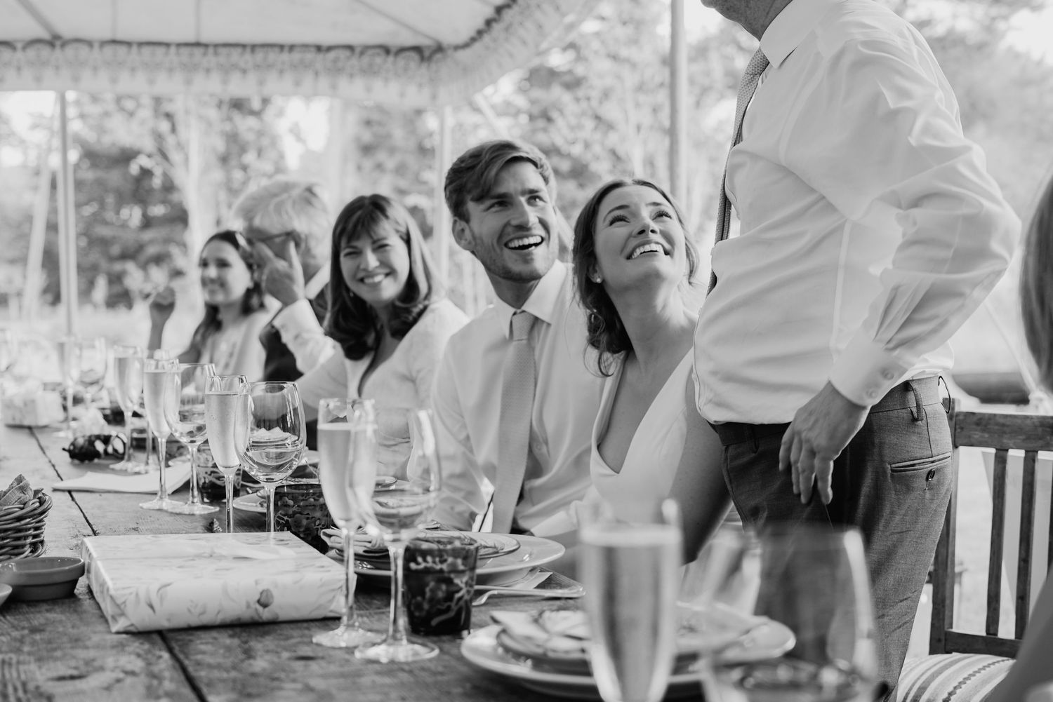 Bride and groom laughing joyfully at a wedding reception table in a black and white photo.