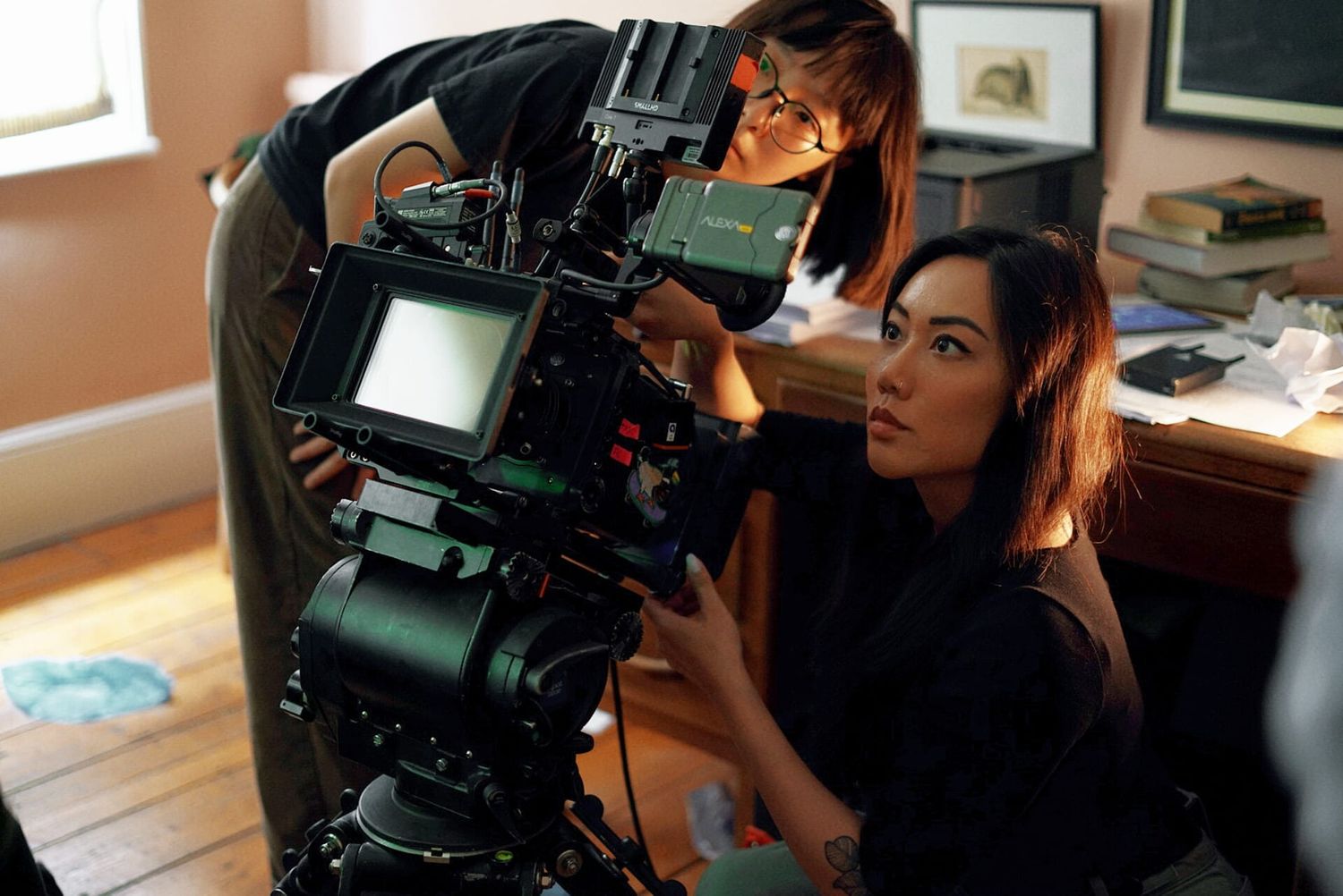 Two women operate a professional film camera on an indoor movie set.