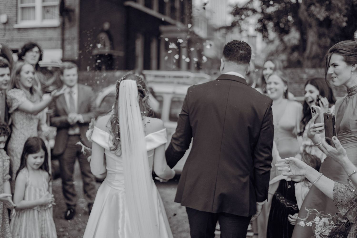 Bride and groom walking through confetti shower in black and white wedding exit photo.