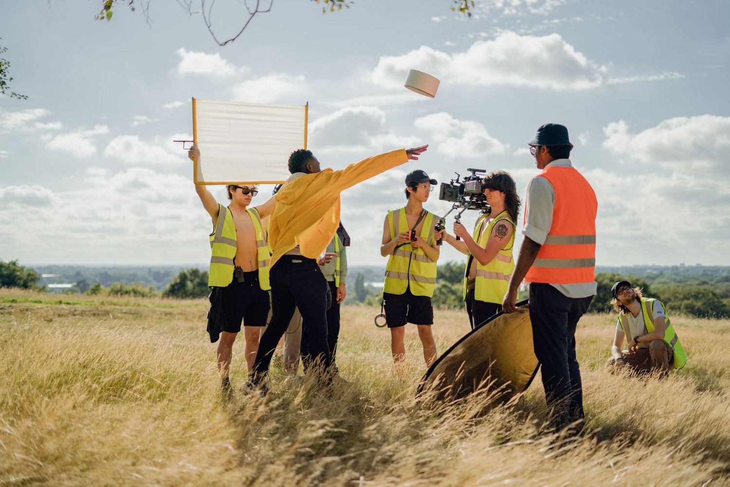 Film crew in yellow high-vis vests working on an outdoor production in a golden wheat field.