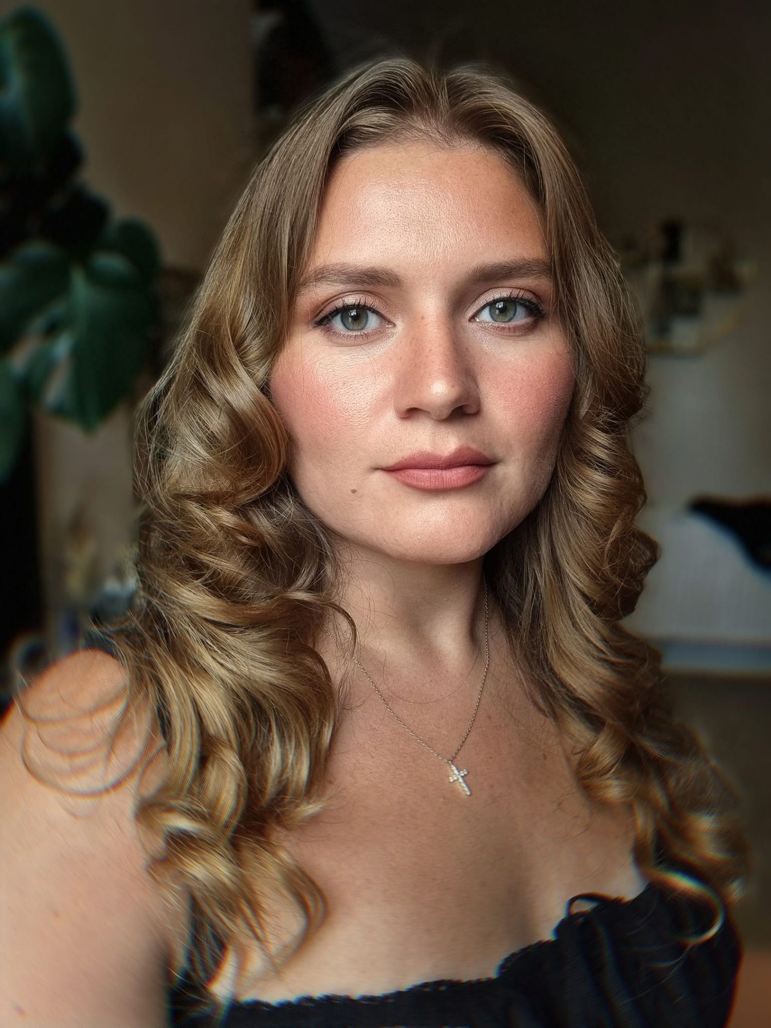Portrait of young woman with wavy blonde hair, freckles, and cross necklace in natural light.