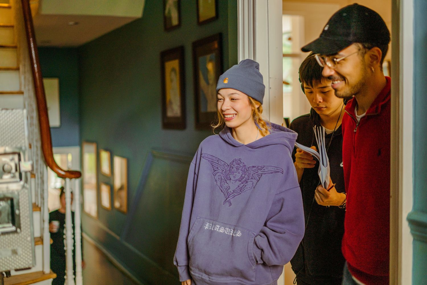 Three young people smile while standing in the doorway of a teal-painted house.