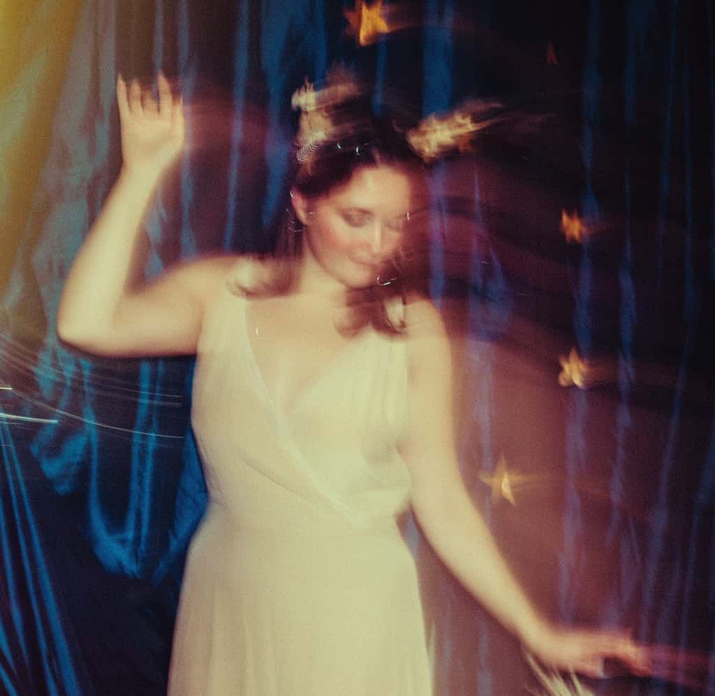 Woman in white dress dancing with motion blur and golden star bokeh effects in blue light.