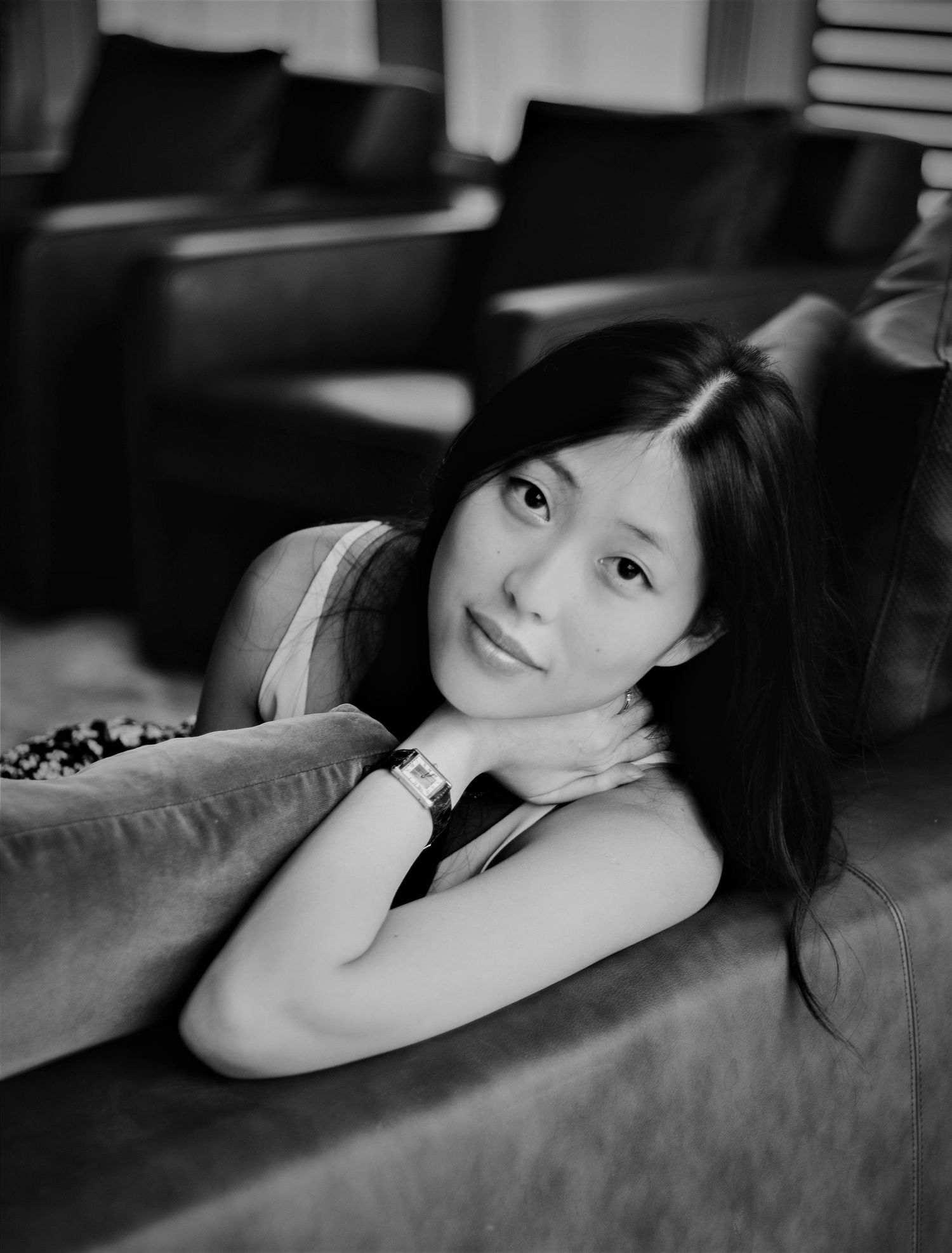 Black and white photo of smiling Asian woman lying on sofa with hand under chin.