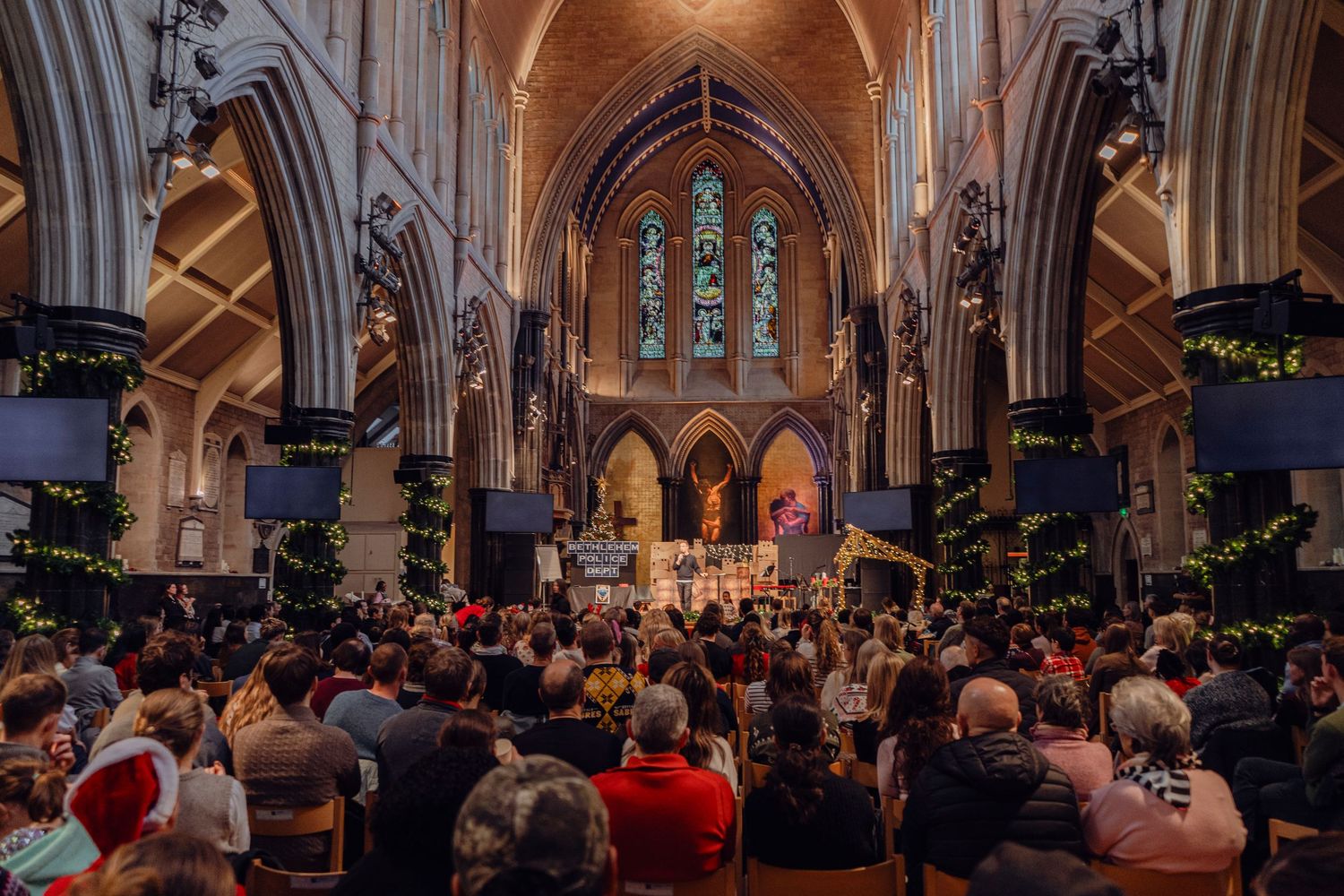 A packed congregation fills a stunning Gothic cathedral decorated for a Christmas service.