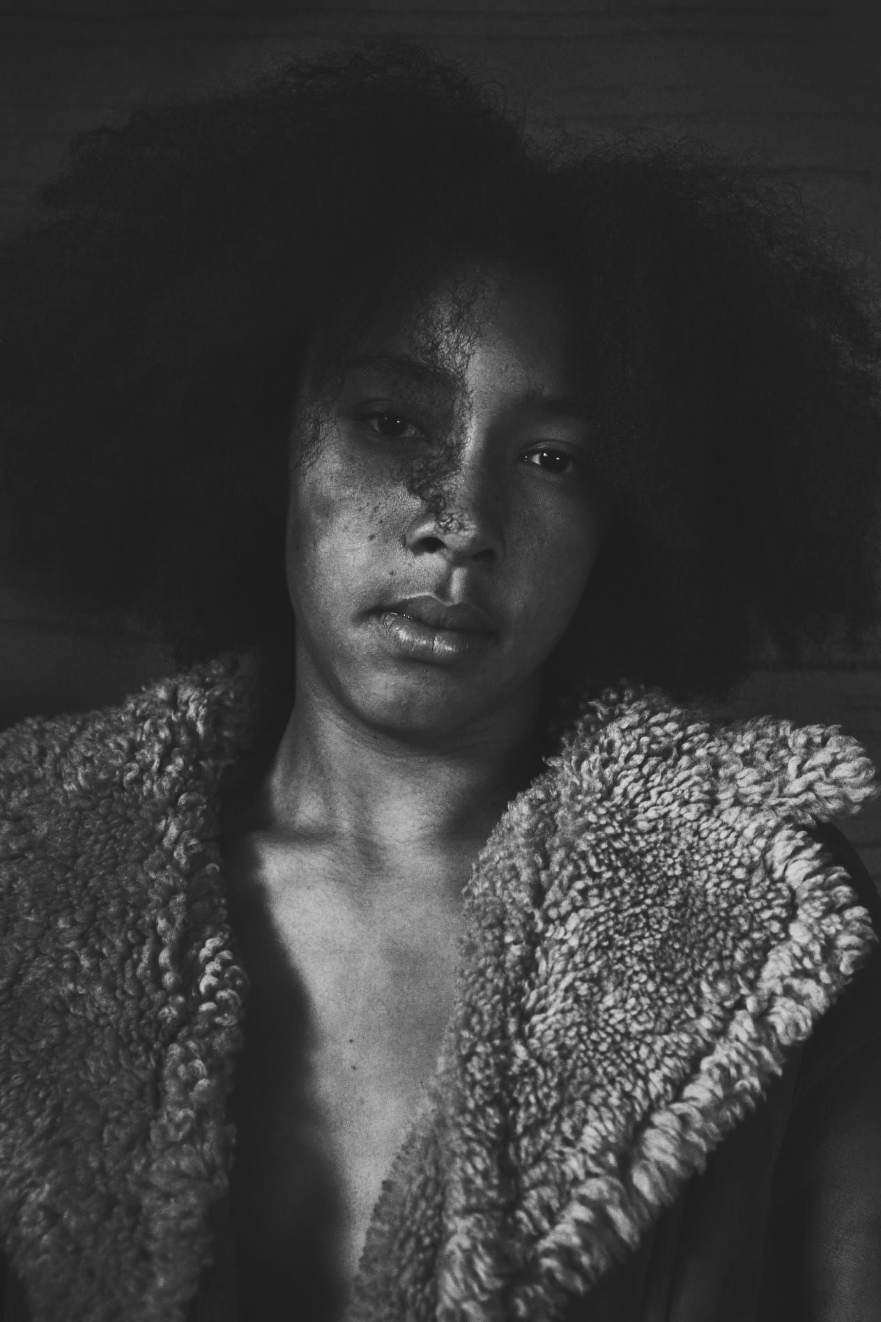 Black and white portrait of a young woman in a fluffy coat with dramatic lighting.