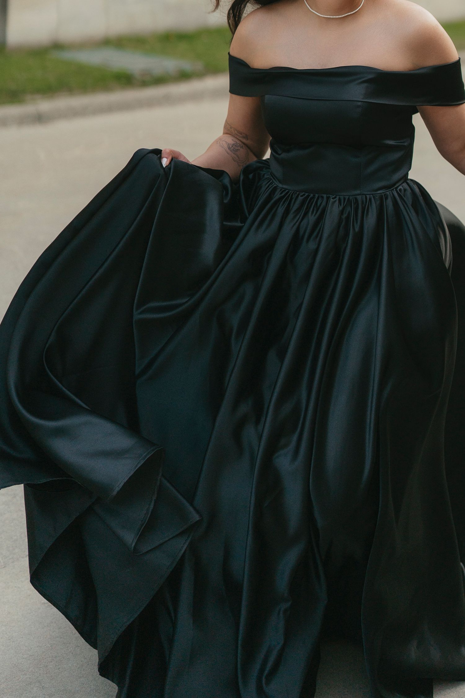 Close-up of a flowing black satin ball gown with an off-the-shoulder neckline moving as the wearer walks down a street.