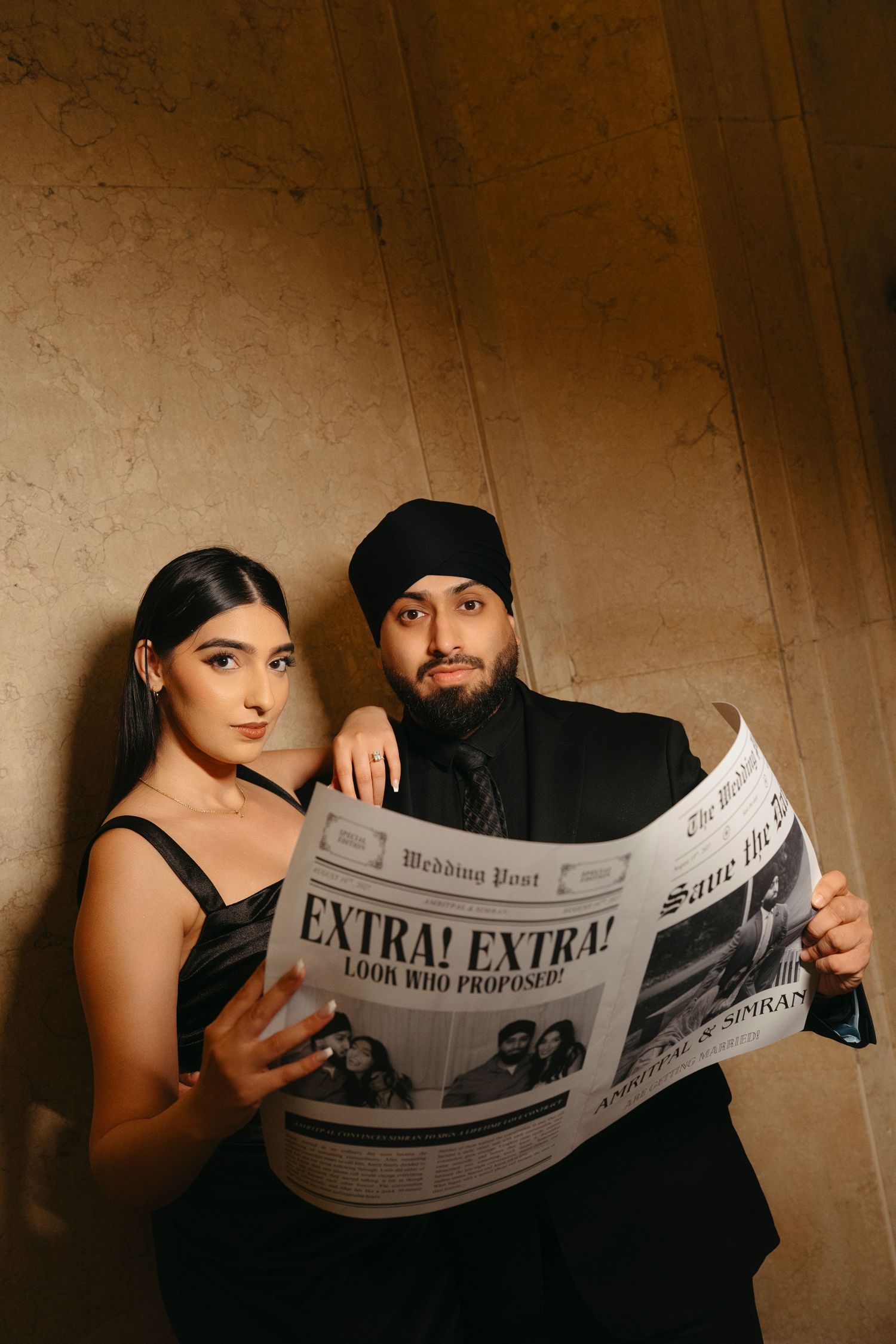 Couple in black pose together holding a Wedding Post newspaper with an Extra Extra who proposed headline for their save the date.