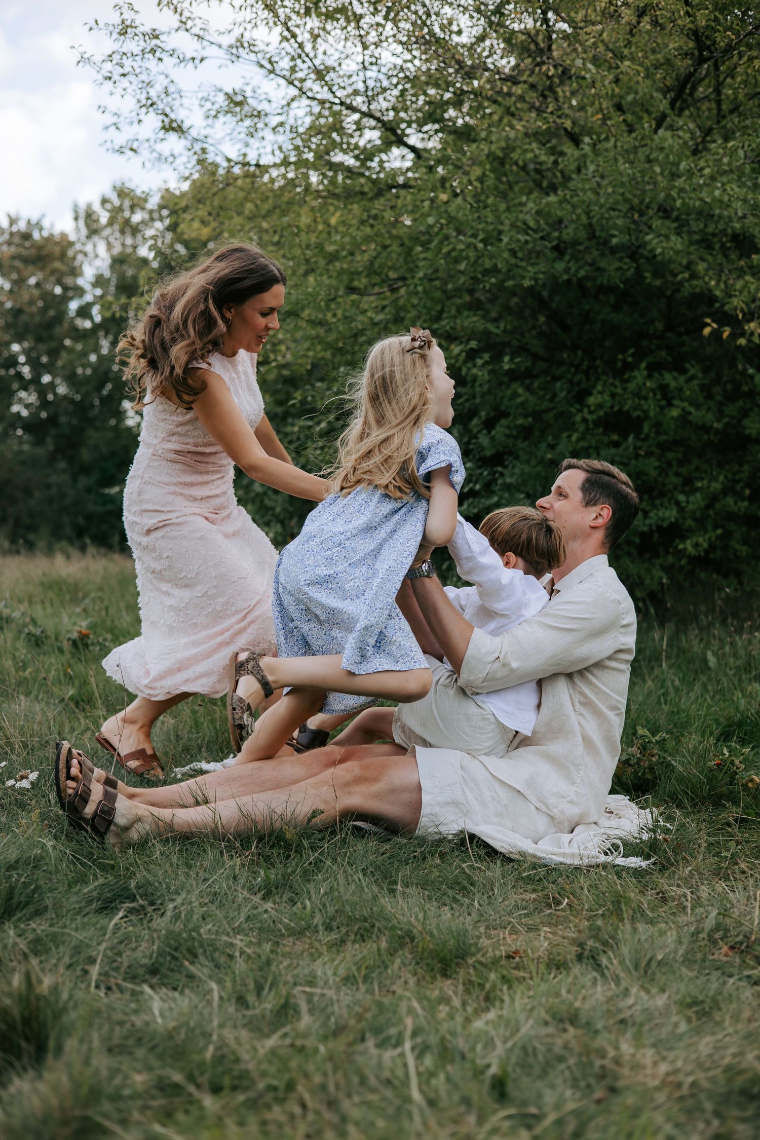 Joyful family of four playing and laughing together on a grassy meadow outdoors.