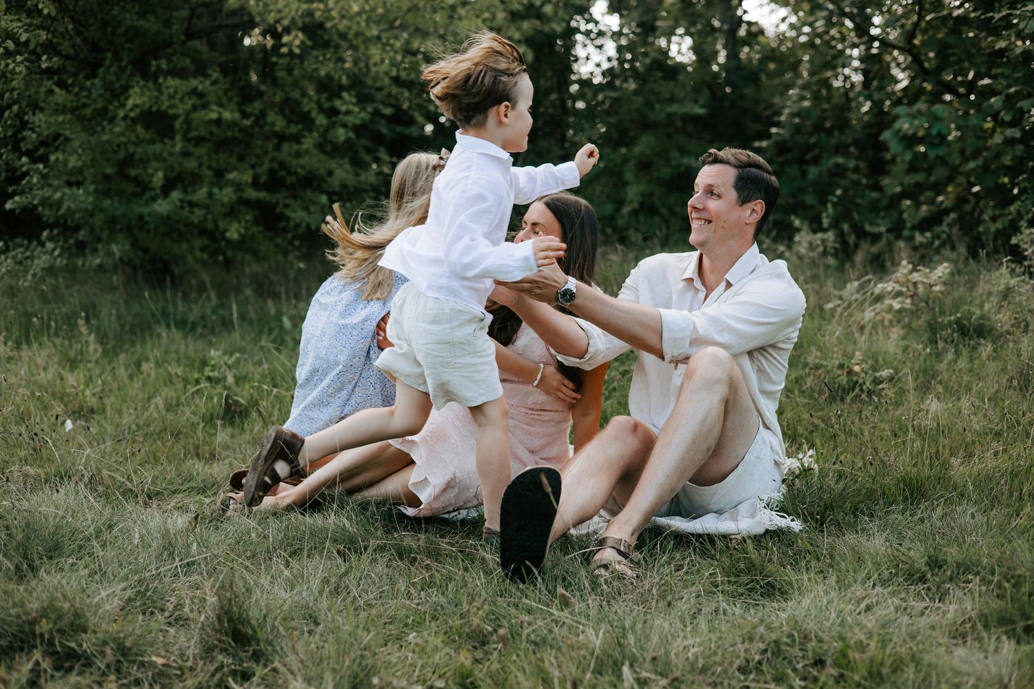Happy family with two young children playing together on grass in lush park.