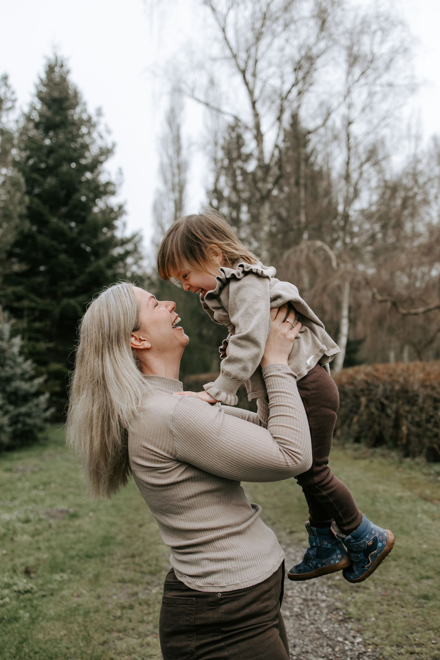 Laughing blonde mother lifting her happy toddler daughter up in an outdoor garden setting.