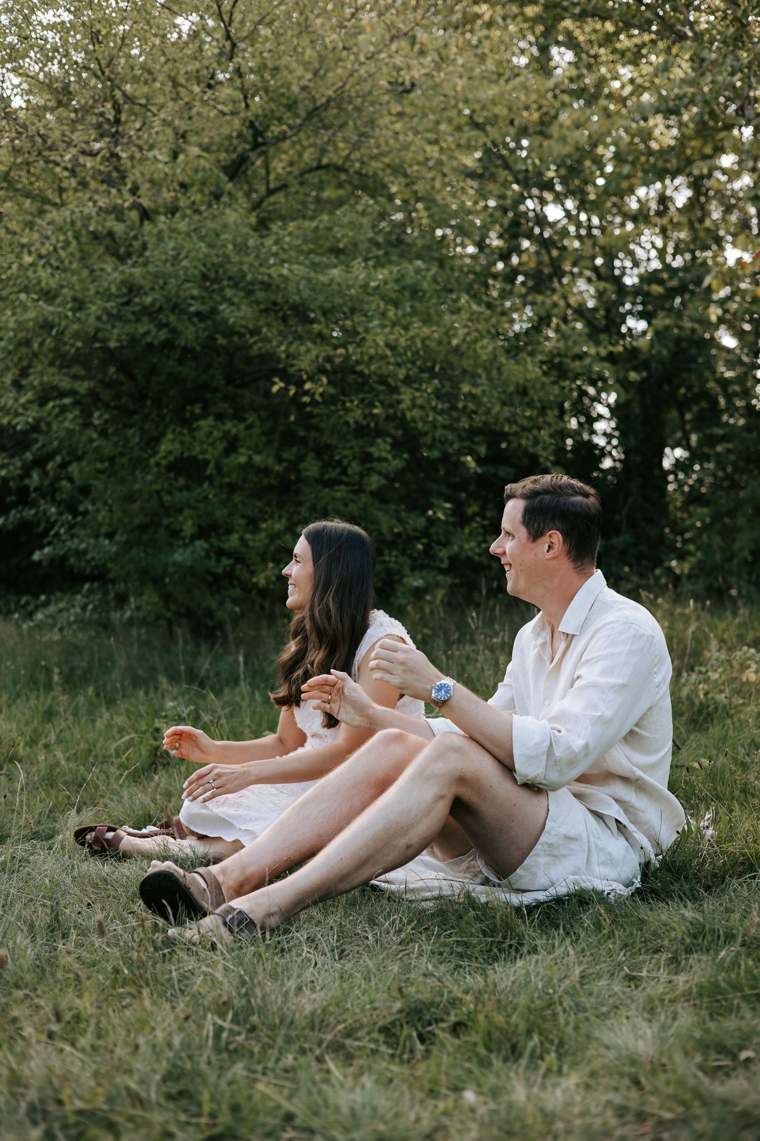 Smiling couple sitting together on green grass in peaceful outdoor natural setting.