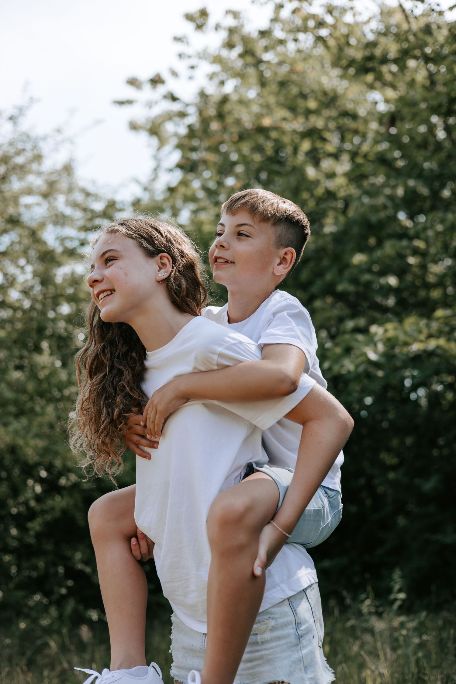 Smiling girl giving her younger brother a piggyback ride outdoors in nature.