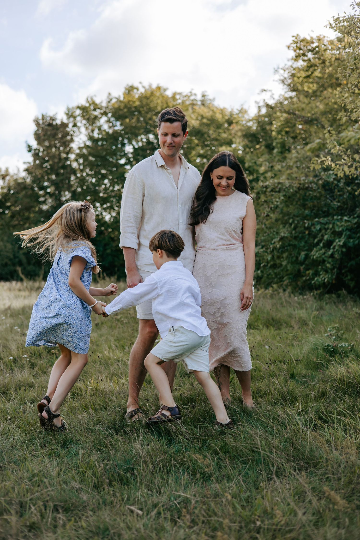 Happy family with two children dancing and playing outdoors in a lush green field.