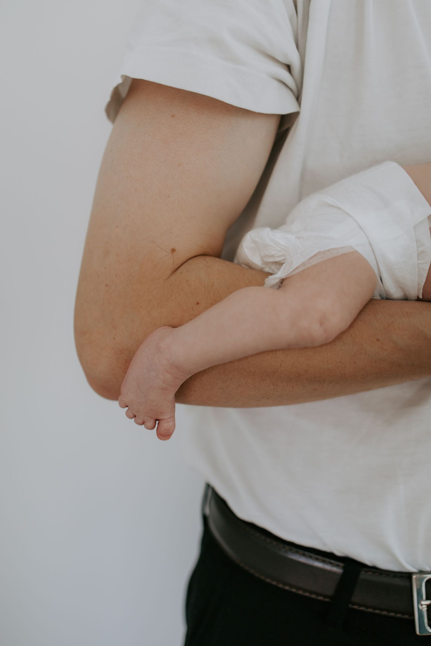 Close-up of a man in a white t-shirt cradling a newborn baby against his chest.