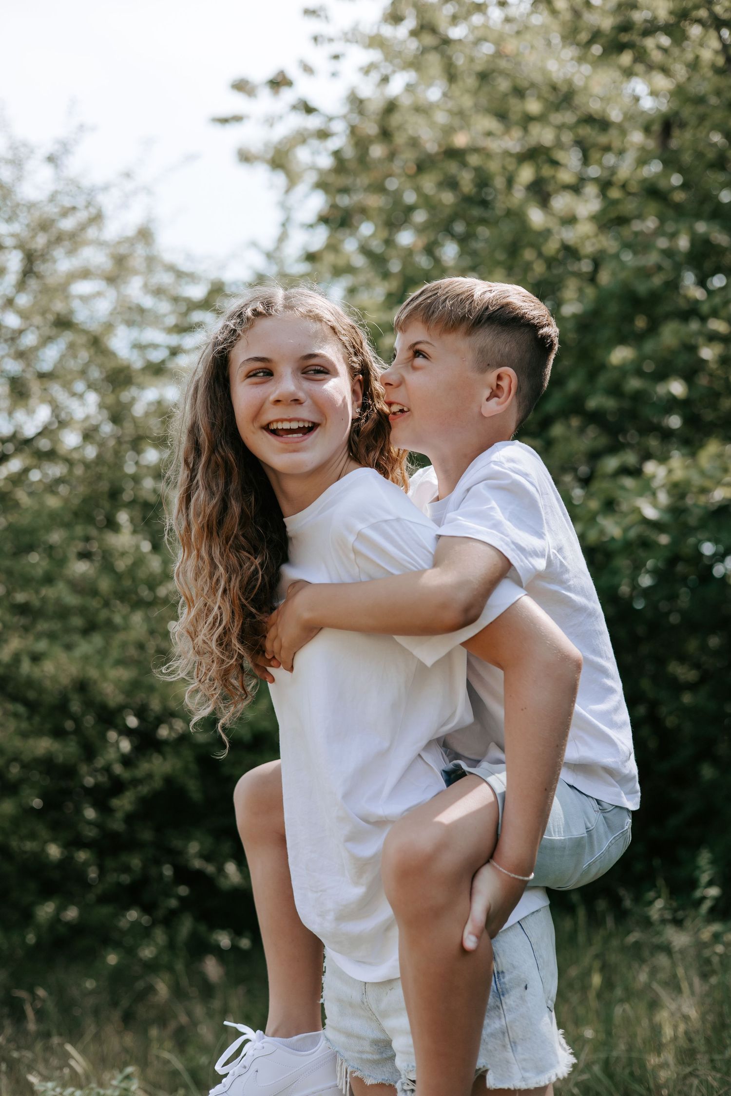 Happy girl giving boy piggyback ride outdoors while he whispers in her ear.
