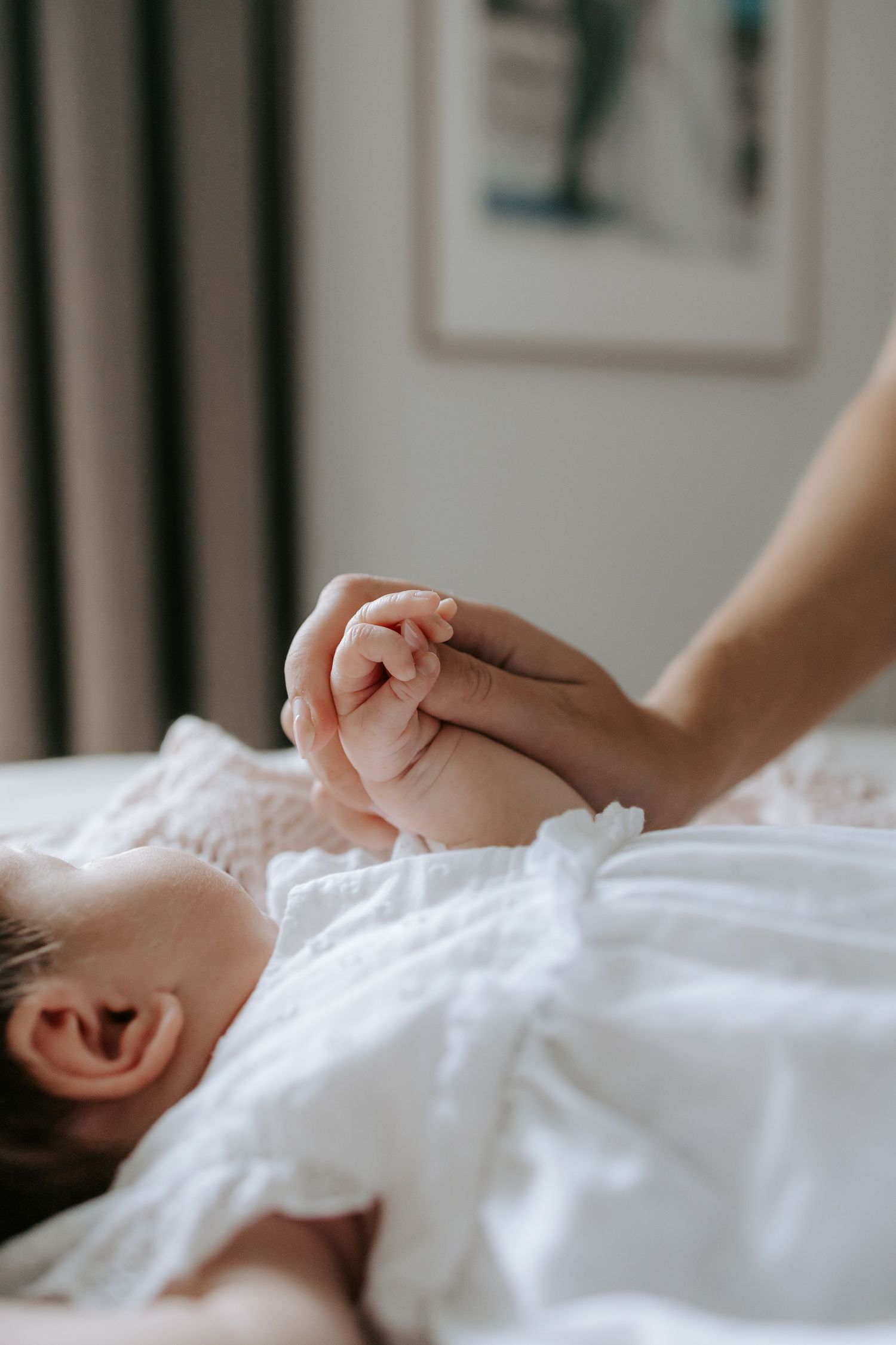 Adult hand gently holding tiny newborn baby fist on white blanket.