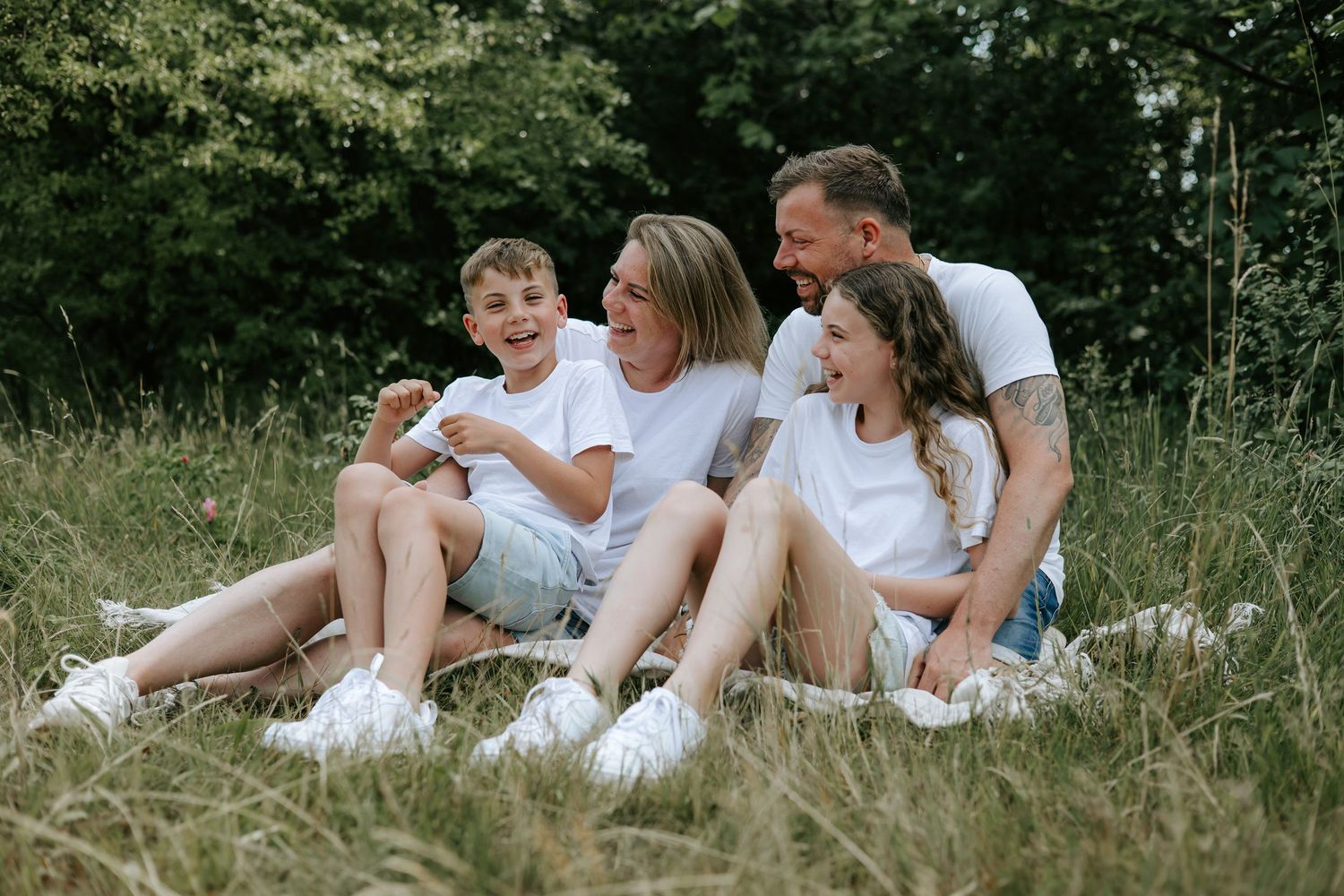 Joyful family of four laughing together on grass, all wearing white shirts in a park.