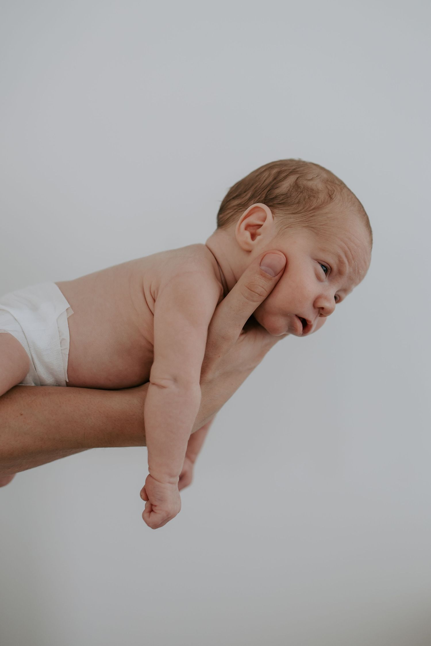 Adult hand supporting a newborn baby lying face-forward against a white background.