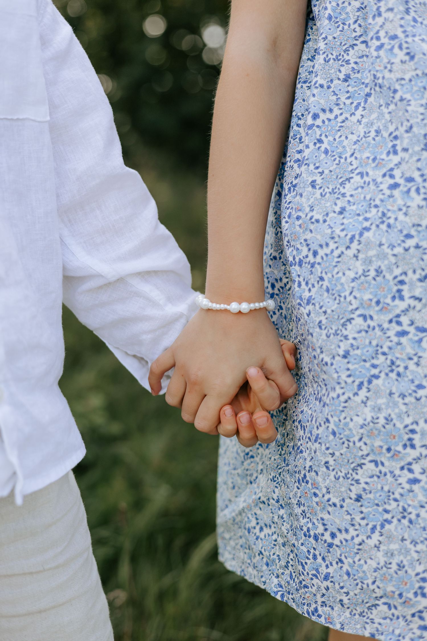 Close-up of two children holding hands, girl wearing a floral bracelet and blue dress.