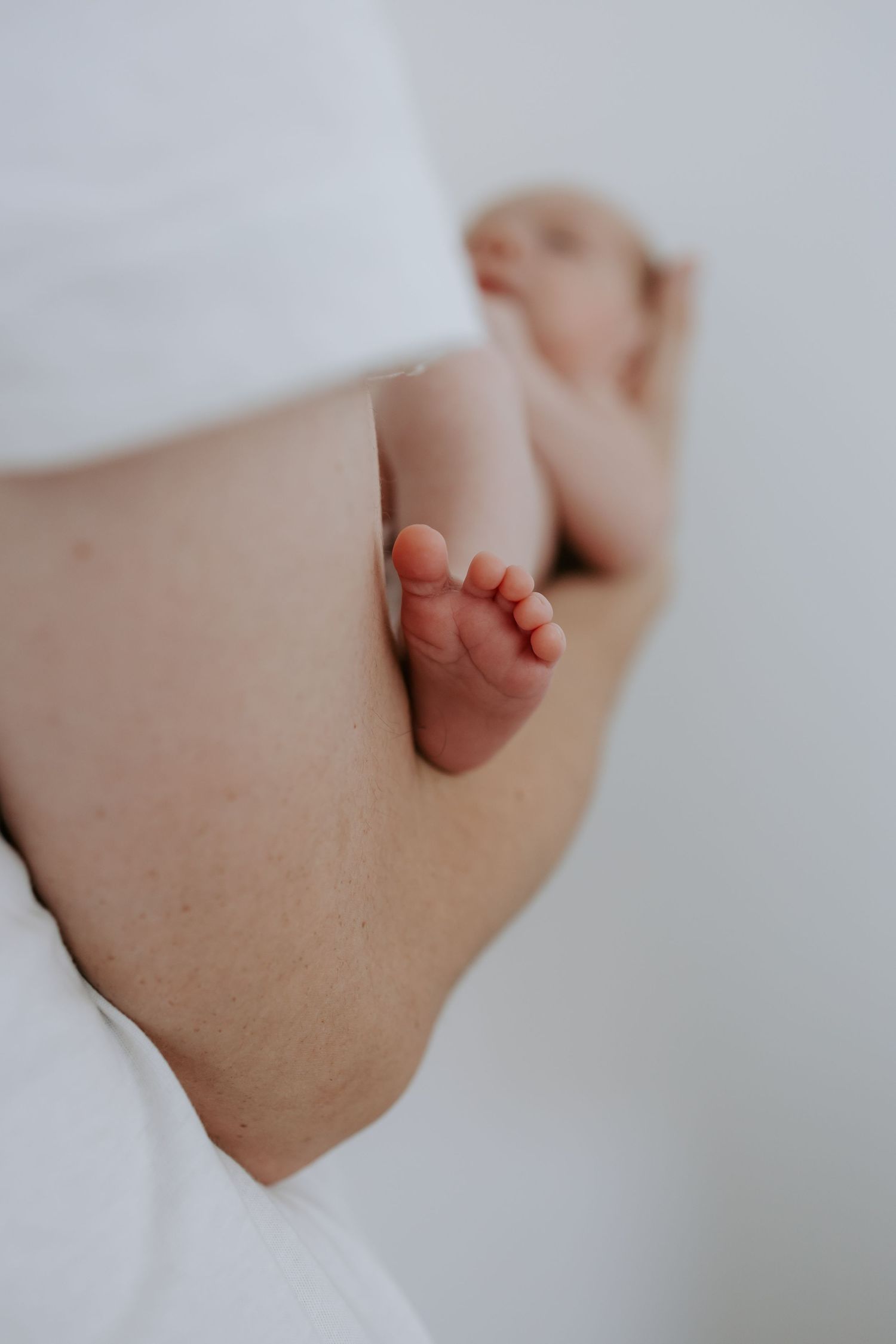 Close-up of tiny newborn baby feet resting against mother's side.