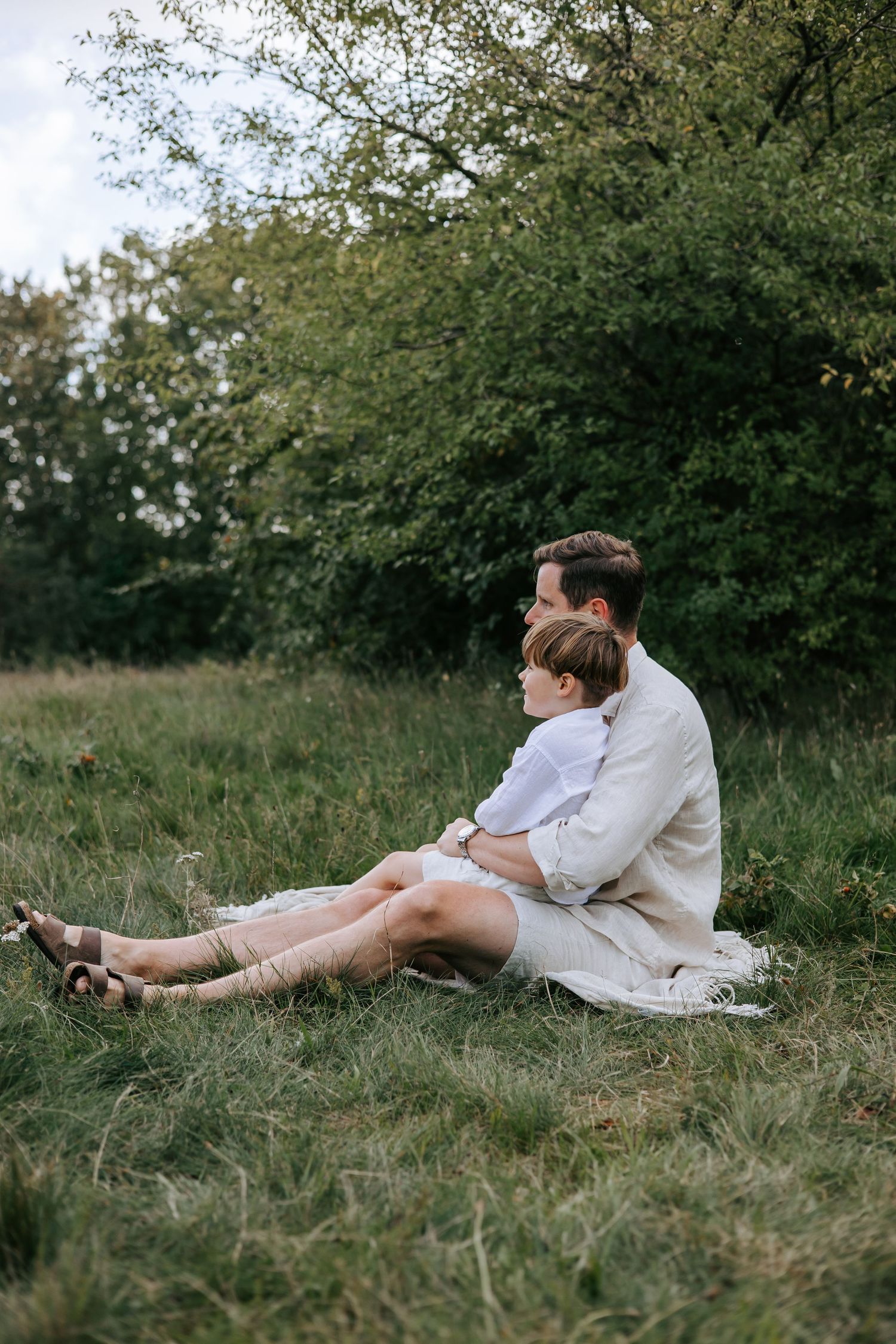 Father and son sitting together on grass in a green field, sharing a quiet moment.