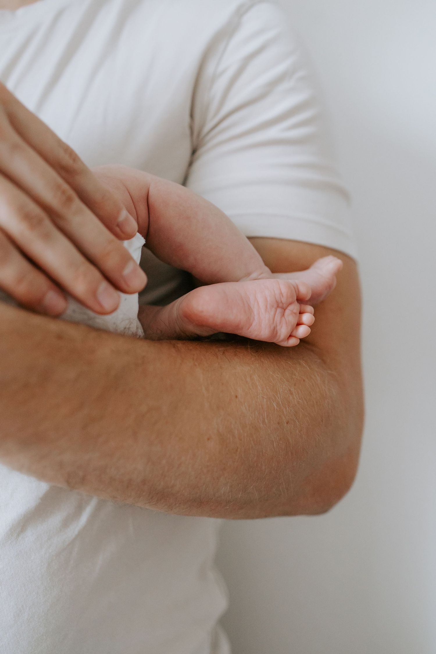 Father holding tiny newborn baby feet in his arms wearing white t-shirt.