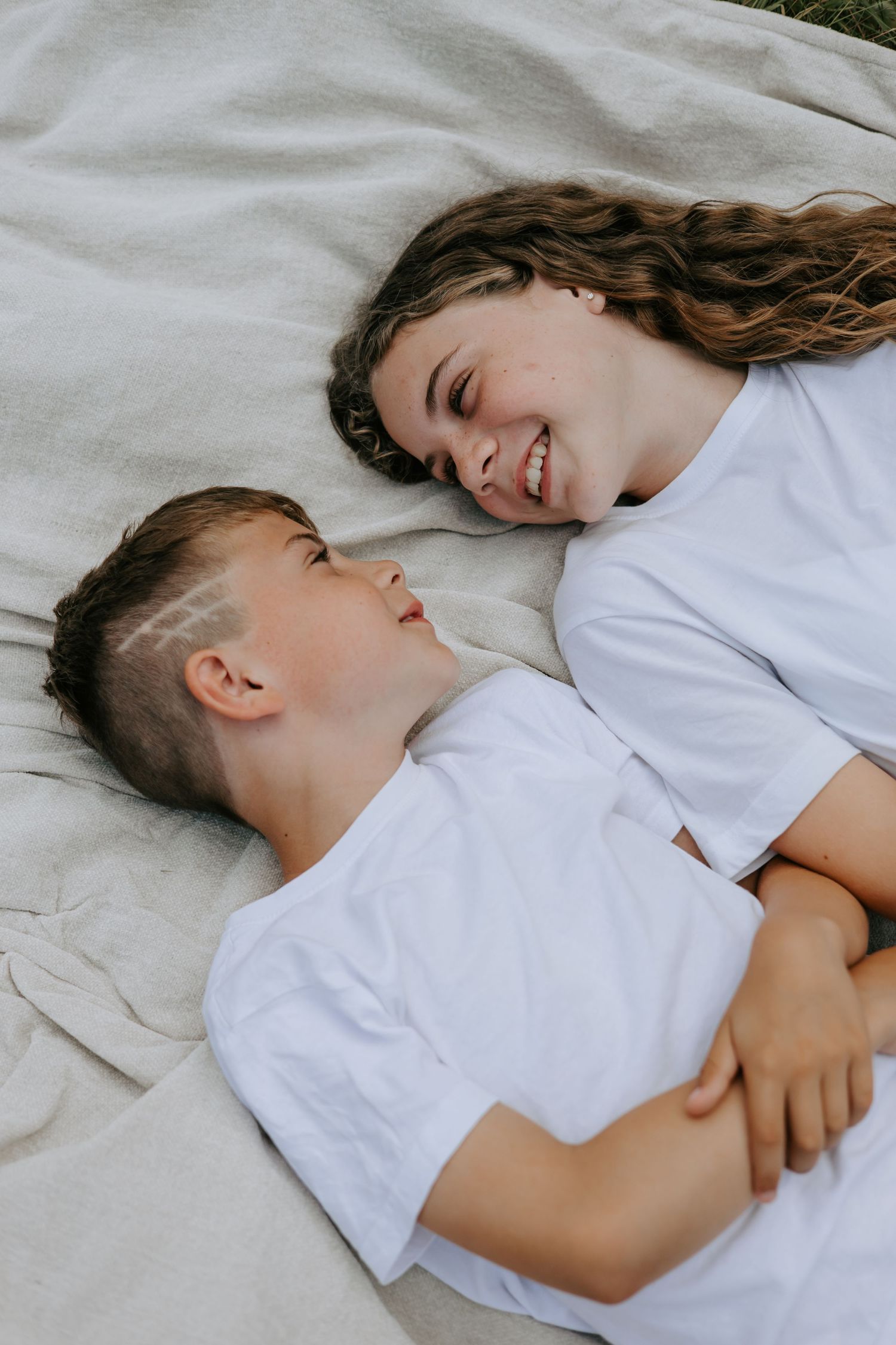 Smiling teenage girl and young boy lying together on blanket in outdoor setting.