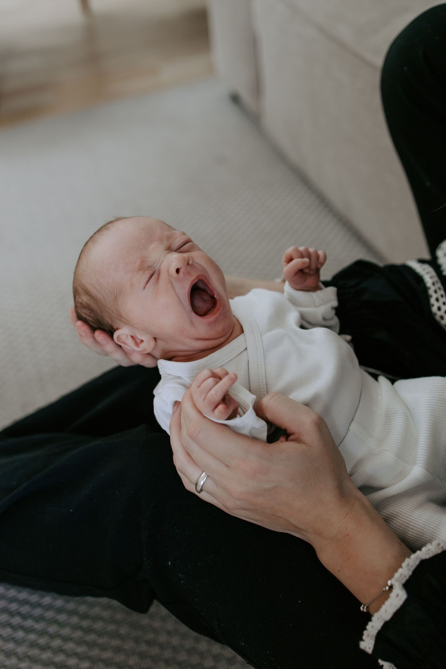 Newborn baby yawning widely while being held by a parent in a bright home.
