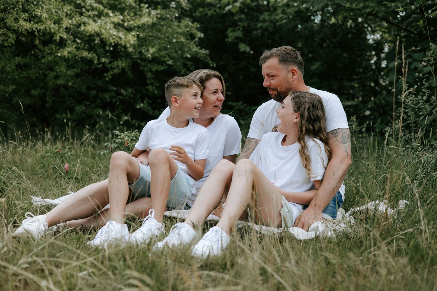 Happy family of four sitting closely together on grass, smiling and enjoying a sunny day.