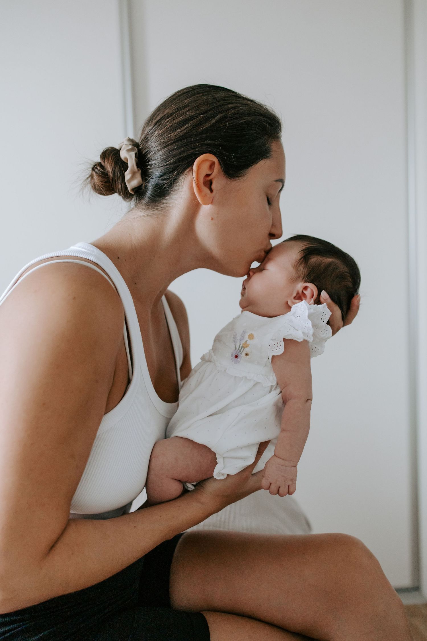 Mother kissing her newborn baby on the forehead while seated indoors.