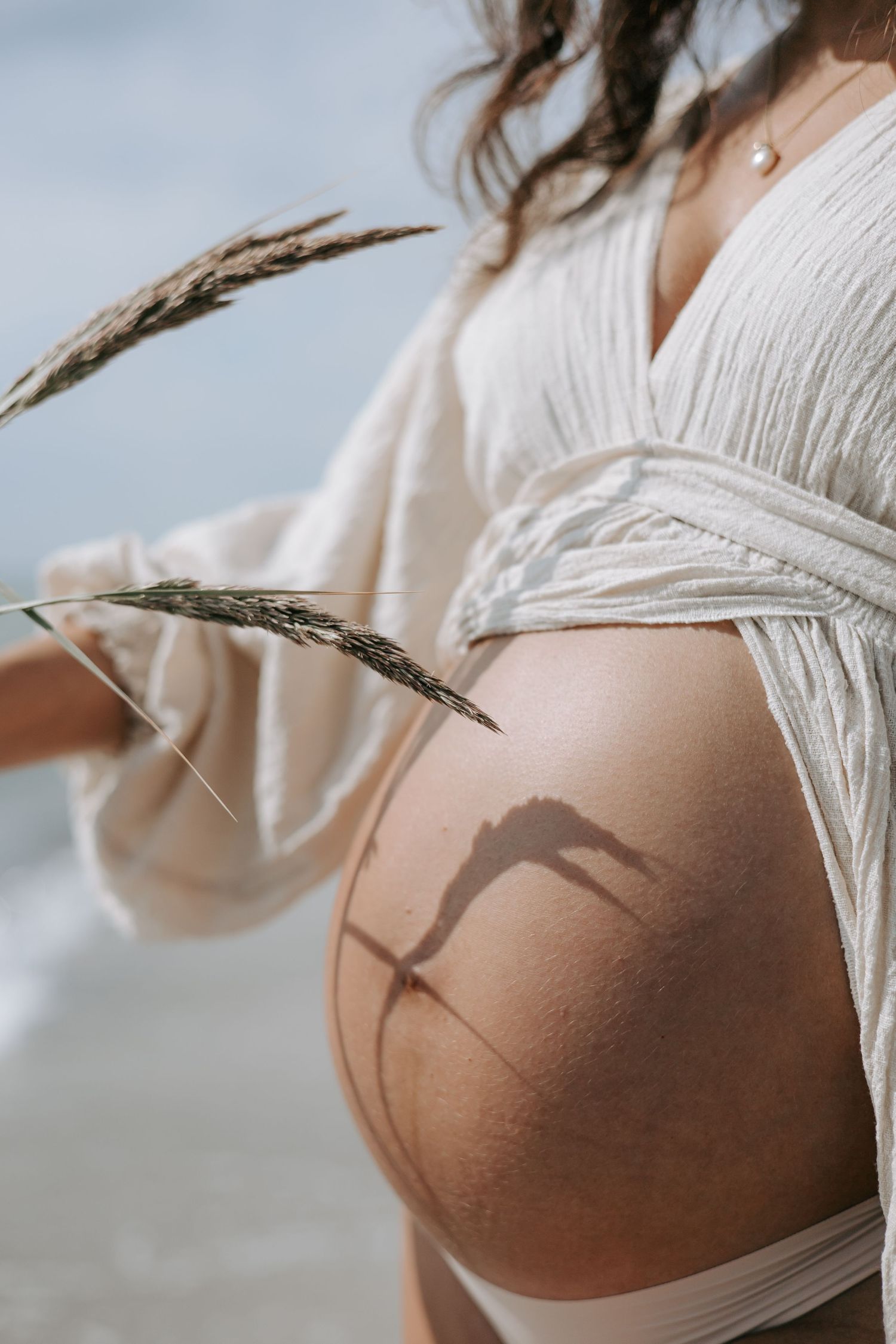 Shadow of wheat grass on pregnant woman's bare belly at beach.