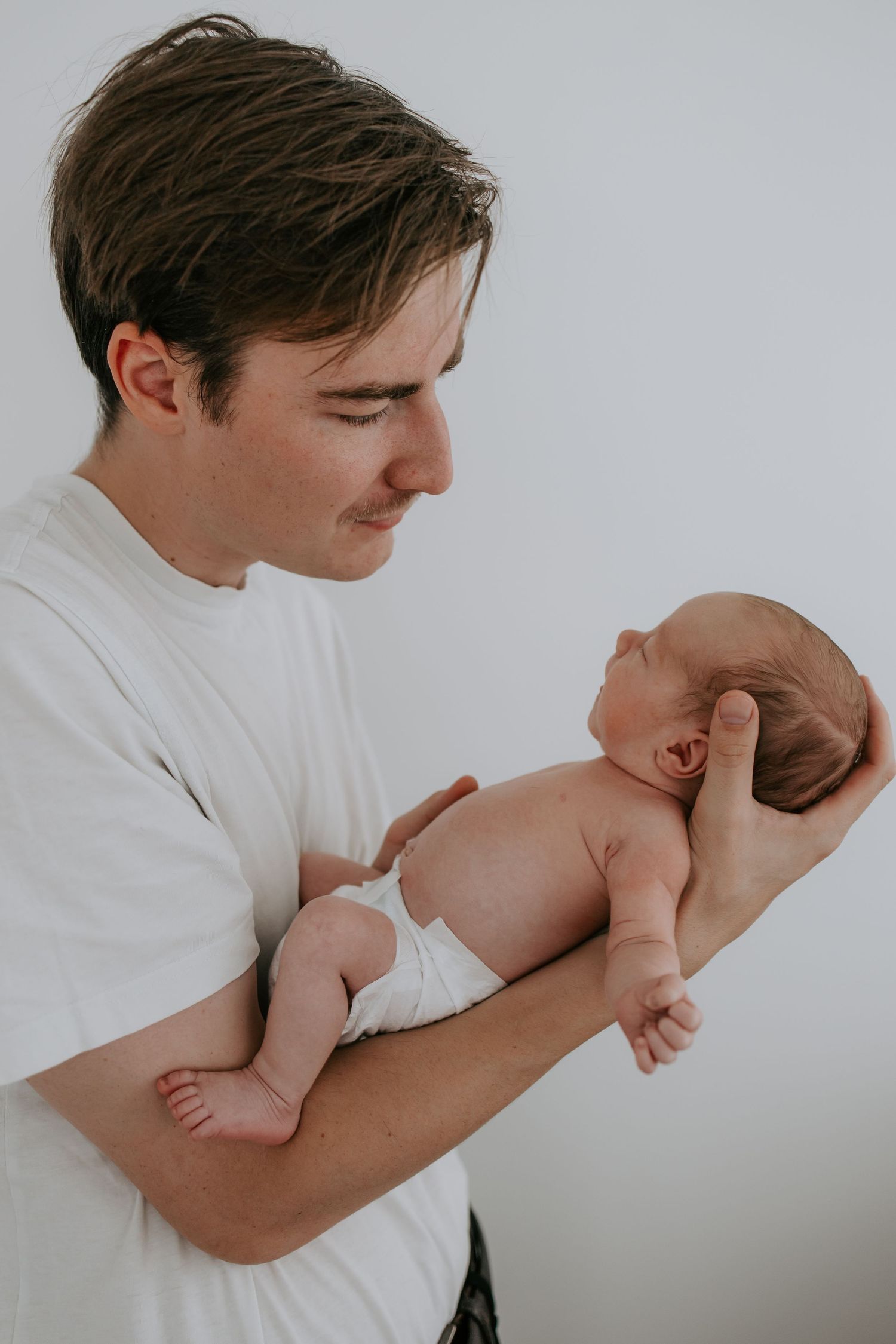 Young father in white t-shirt carefully holding his newborn baby in his arms.