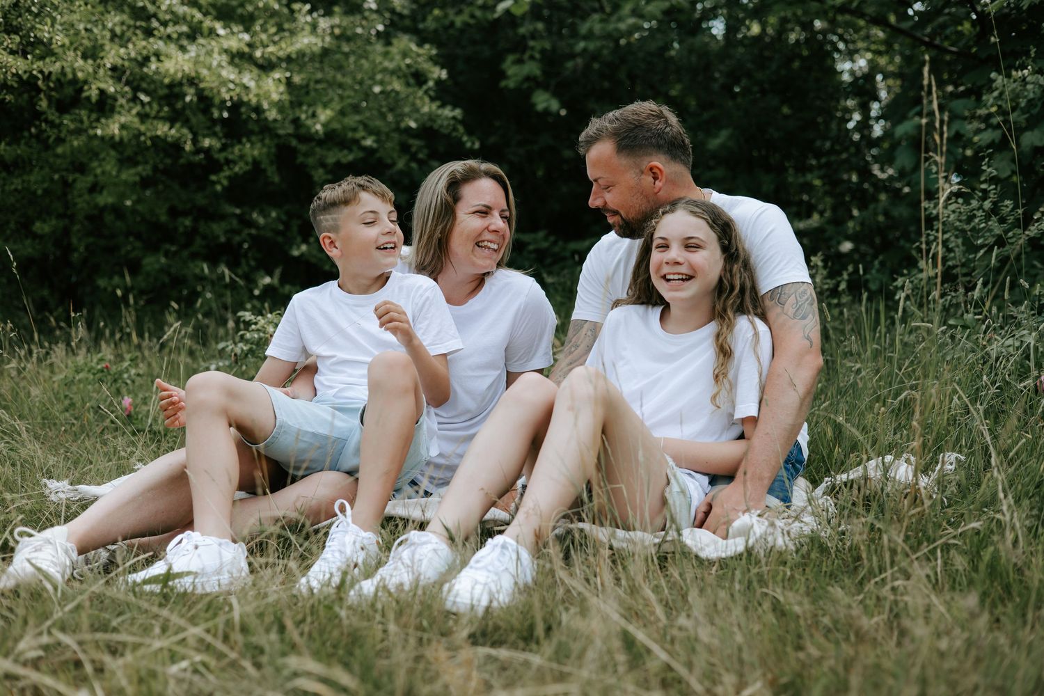 Cheerful family of four relaxing on grass in a park, wearing coordinated white outfits.