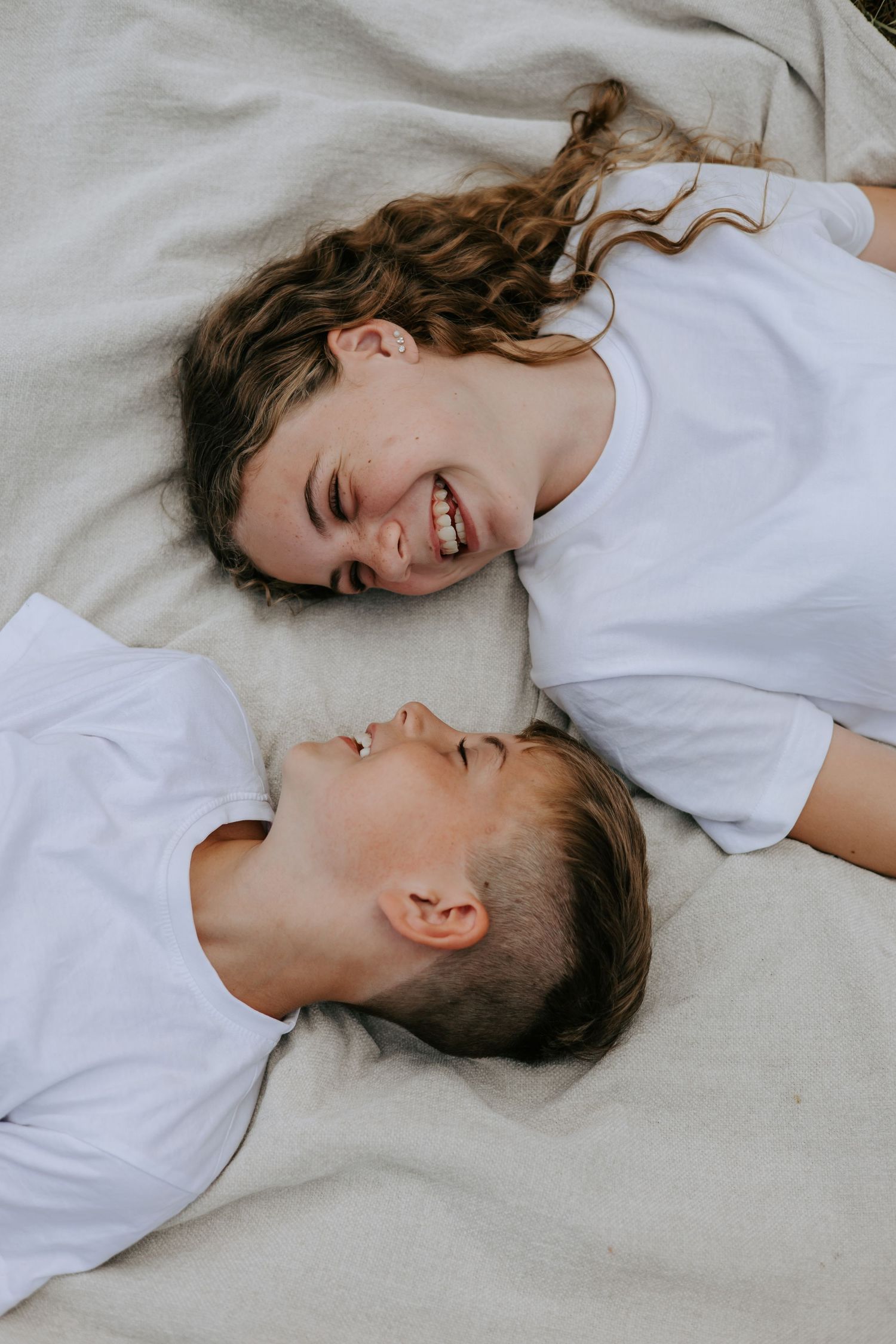 Two laughing children lying on blanket face to face sharing joyful moment outdoors.