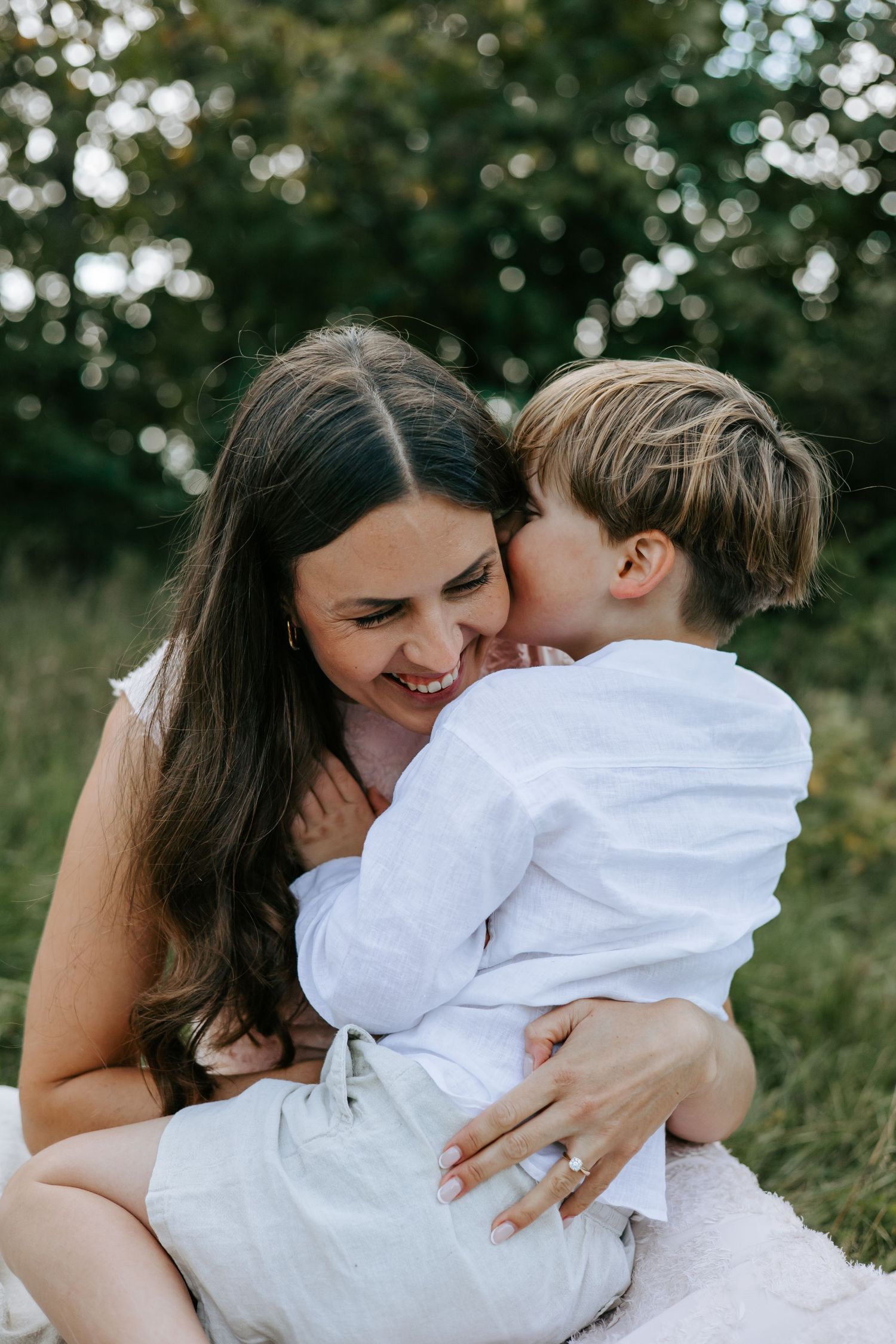 Loving mother smiling as her young son gives her a kiss on the cheek outdoors.
